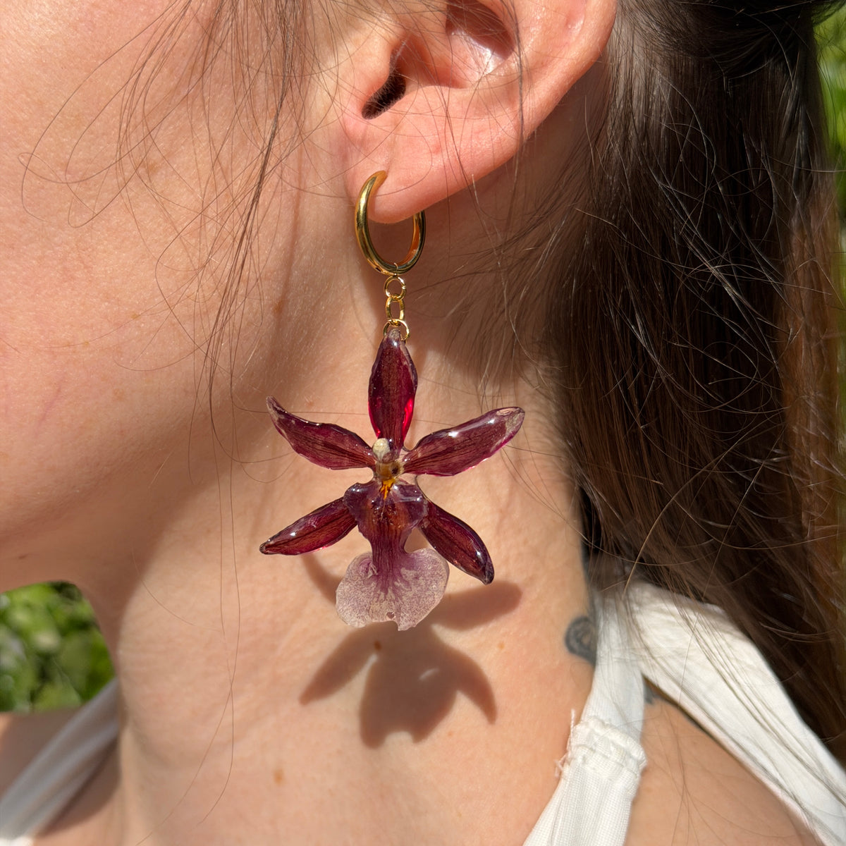 Mujer llevando pendiente de orquídea Cambria burdeos encapsulada en resina, sobre aro de acero inoxidable