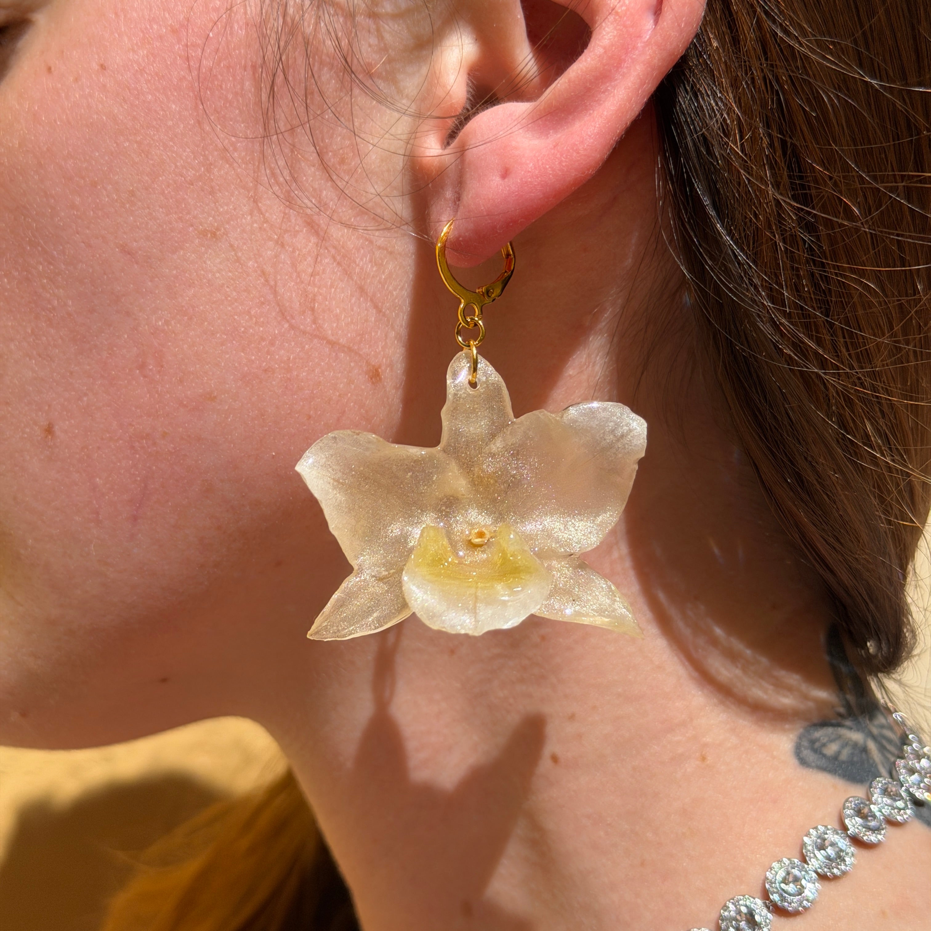 Mujer llevando pendiente de orquídea champán encapsulada en resina sobre la oreja