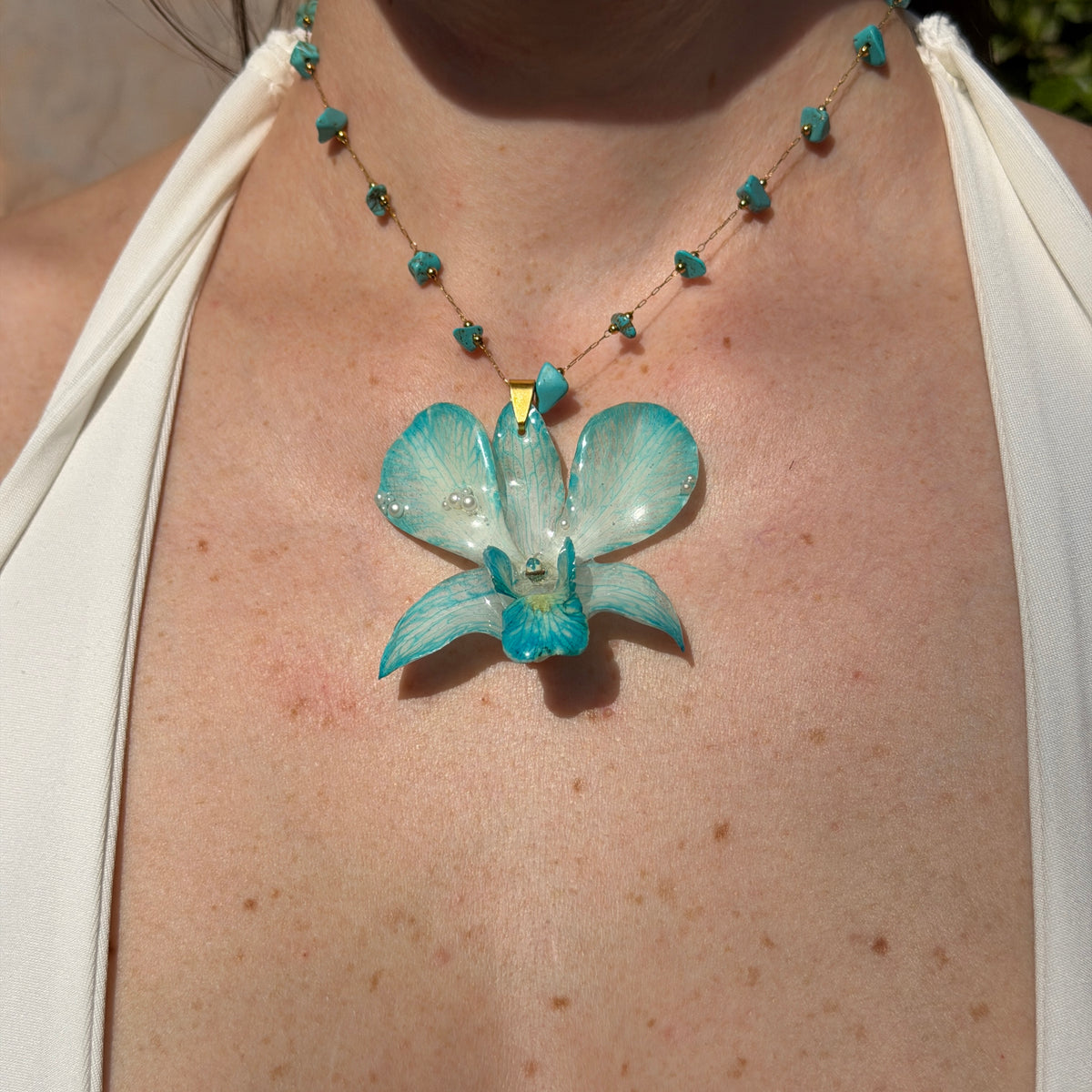 Mujer llevando collar de orquídea Dendrobium turquesa encapsulada en resina, sobre cadena de turquesas