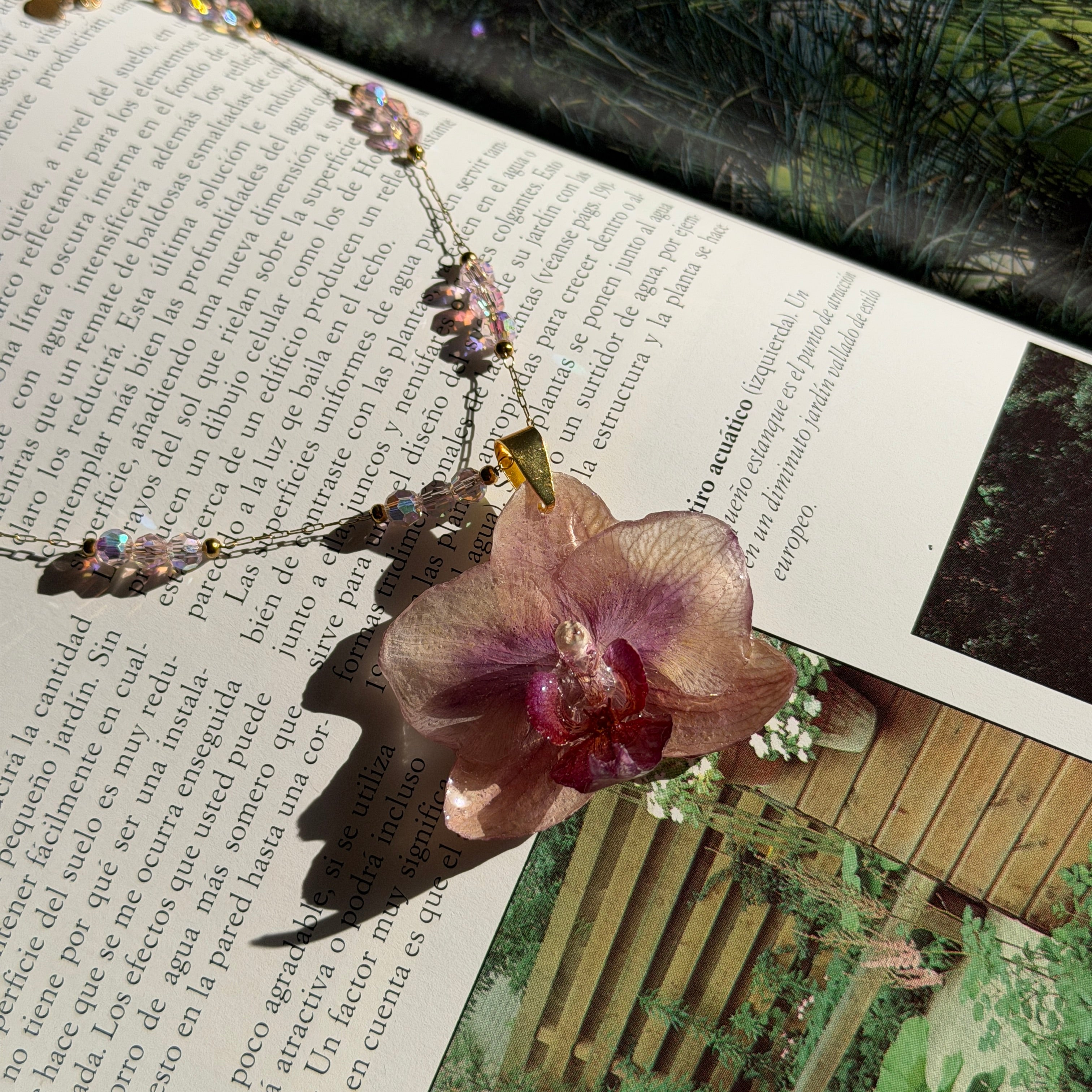 Collar de orquídea rosa encapsulada en resina sobre una revista abierta de jardines