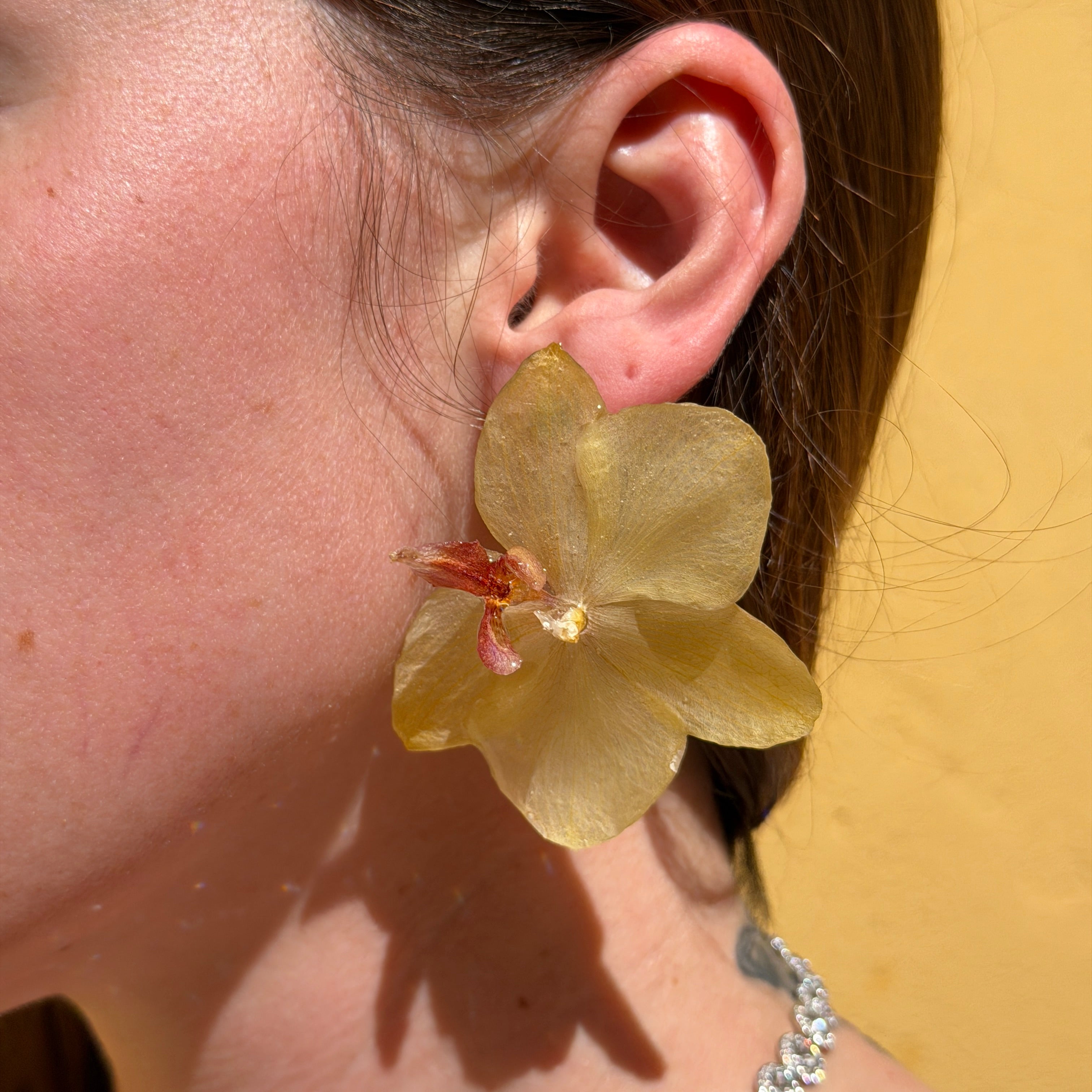 Mujer llevando pendiente de orquídea amarilla encapsulada en resina sobre la oreja