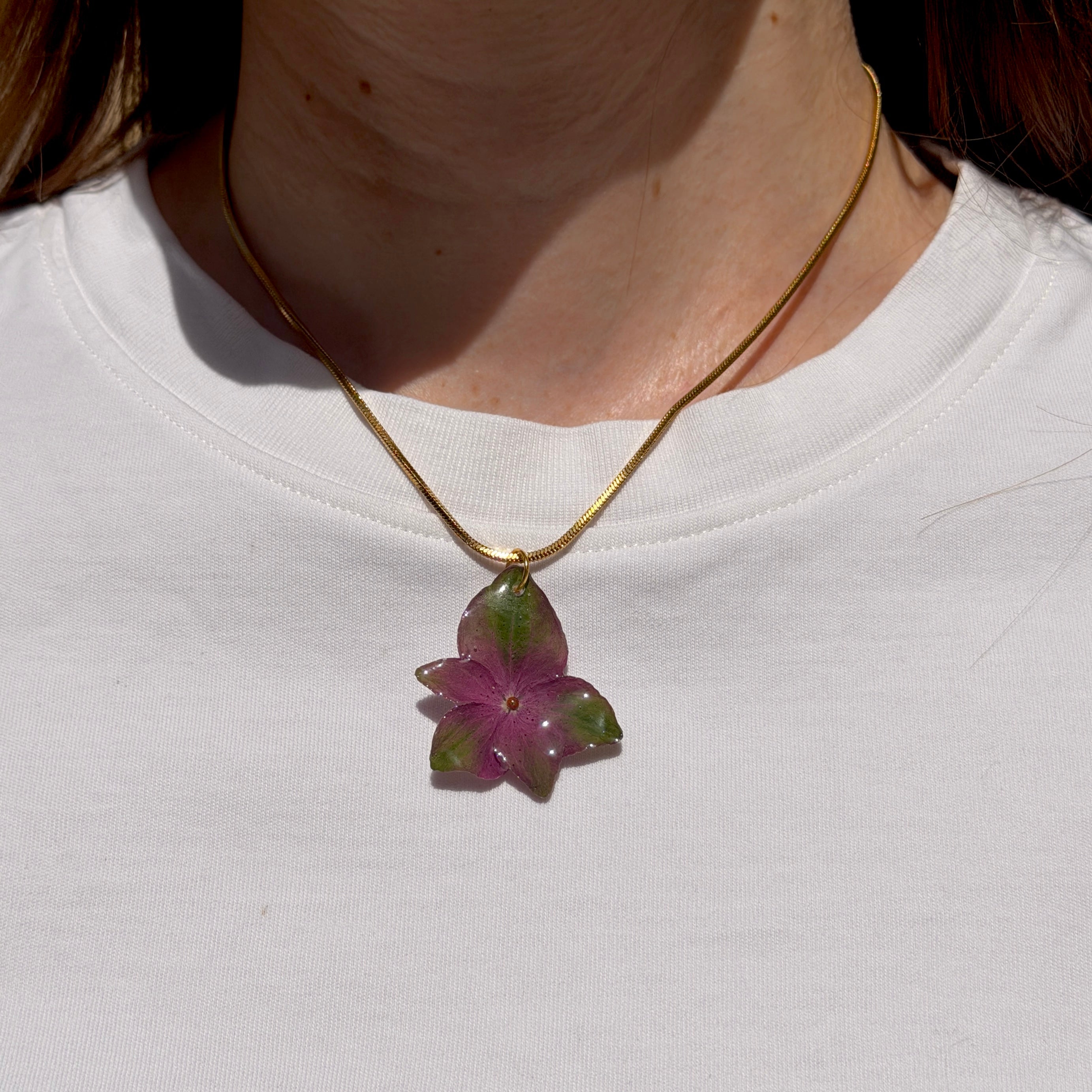 Collar con hortensia morada y verde encapsulada en resina, sobre cadena de acero inoxidable tipo serpiente