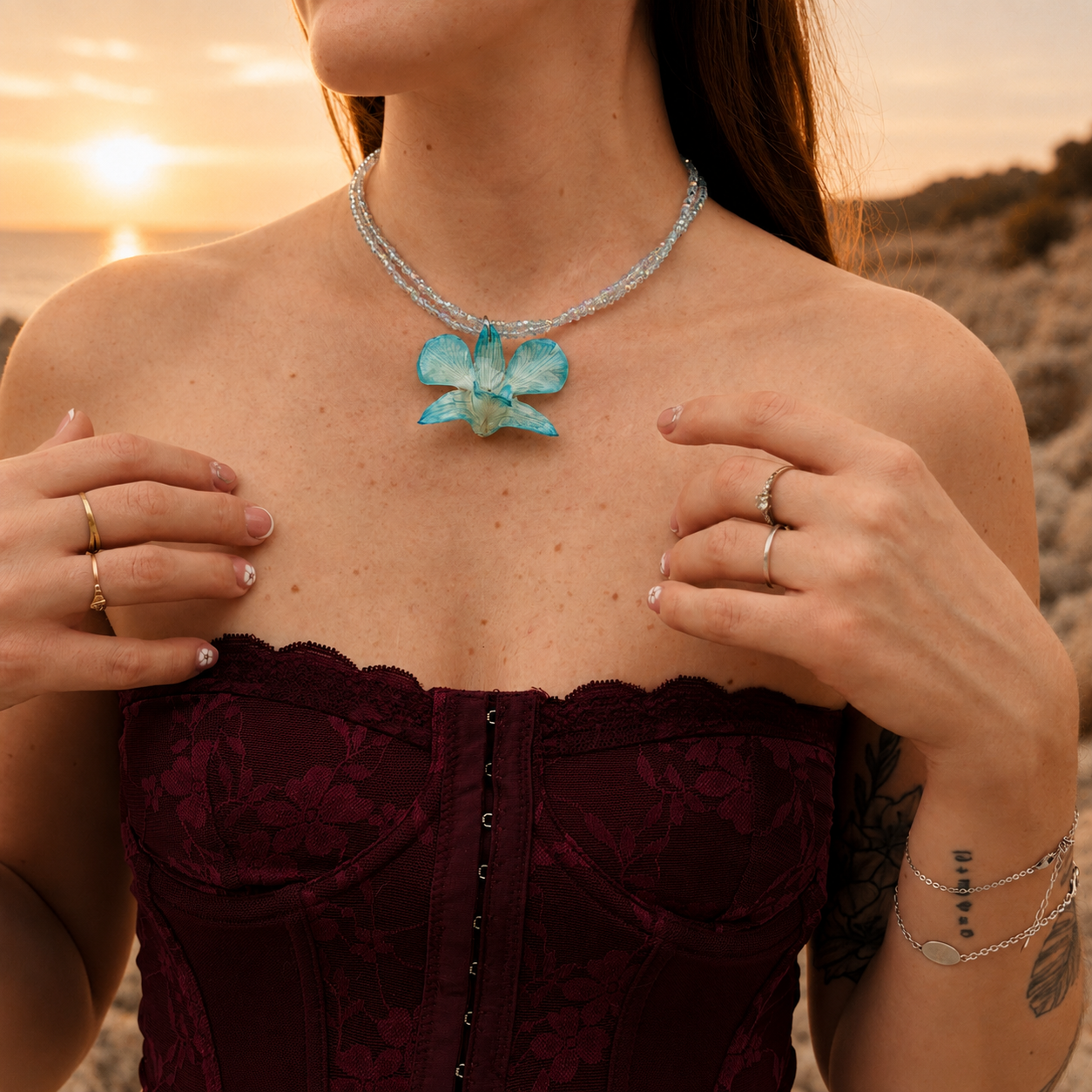 Mujer llevando collar de orquídea turquesa encapsulada en resina sobre el escote, al atardecer junto al mar