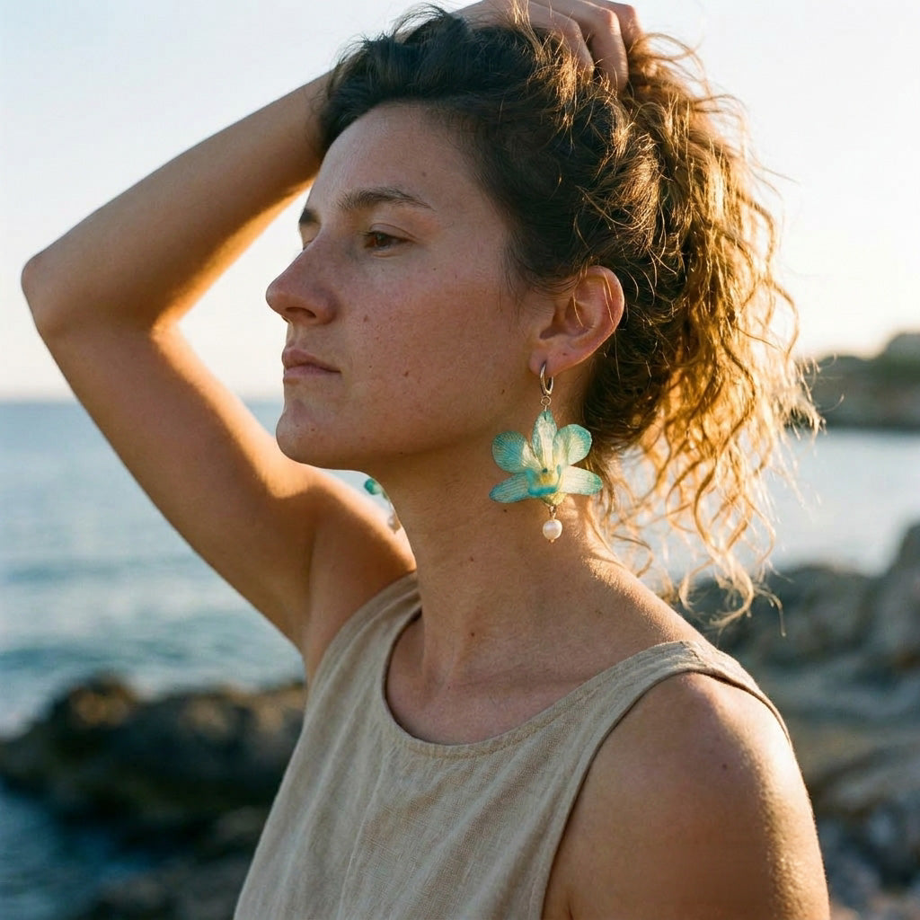 Modelo con pendientes de orquídea turquesa y perla natural junto al mar