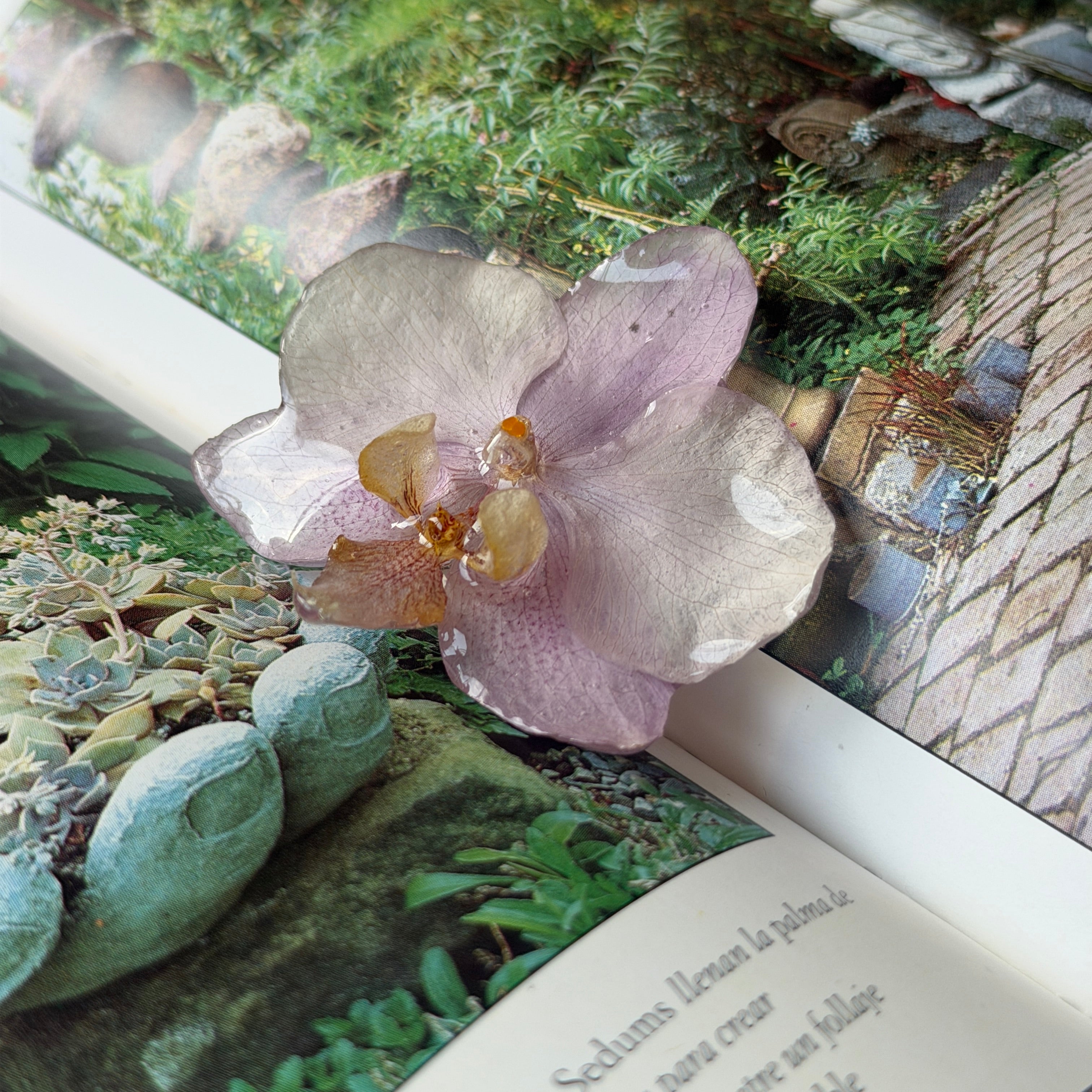 Pinza de orquídea lavanda encapsulada en resina sobre un libro abierto de jardines