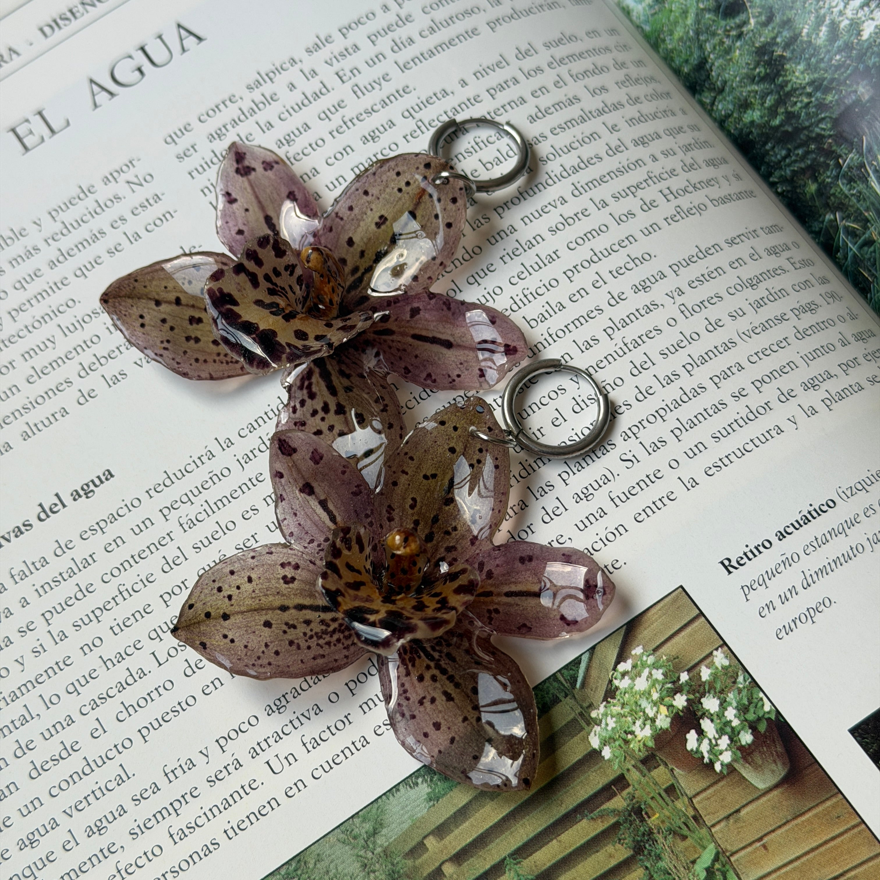 Pendientes de orquídea malva moteada encapsulada en resina, sobre una revista de jardines