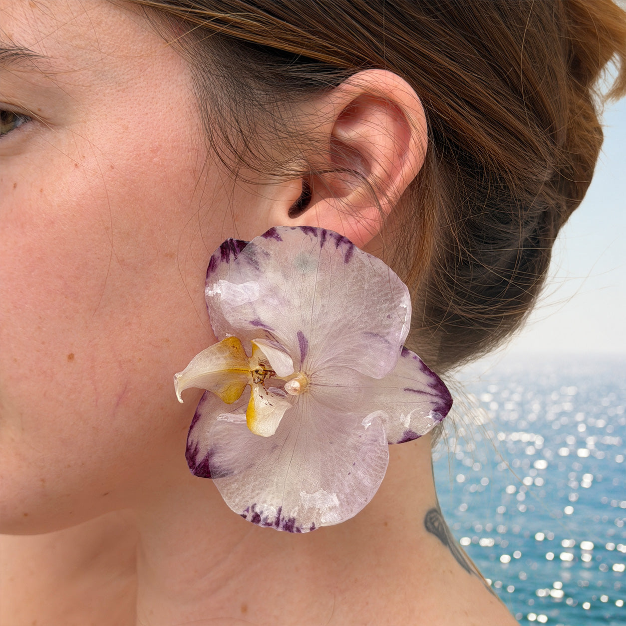 Detalle de orquídea blanco lavanda real preservada en resina, con puntas violeta oscuro y centro amarillo, sobre la oreja
