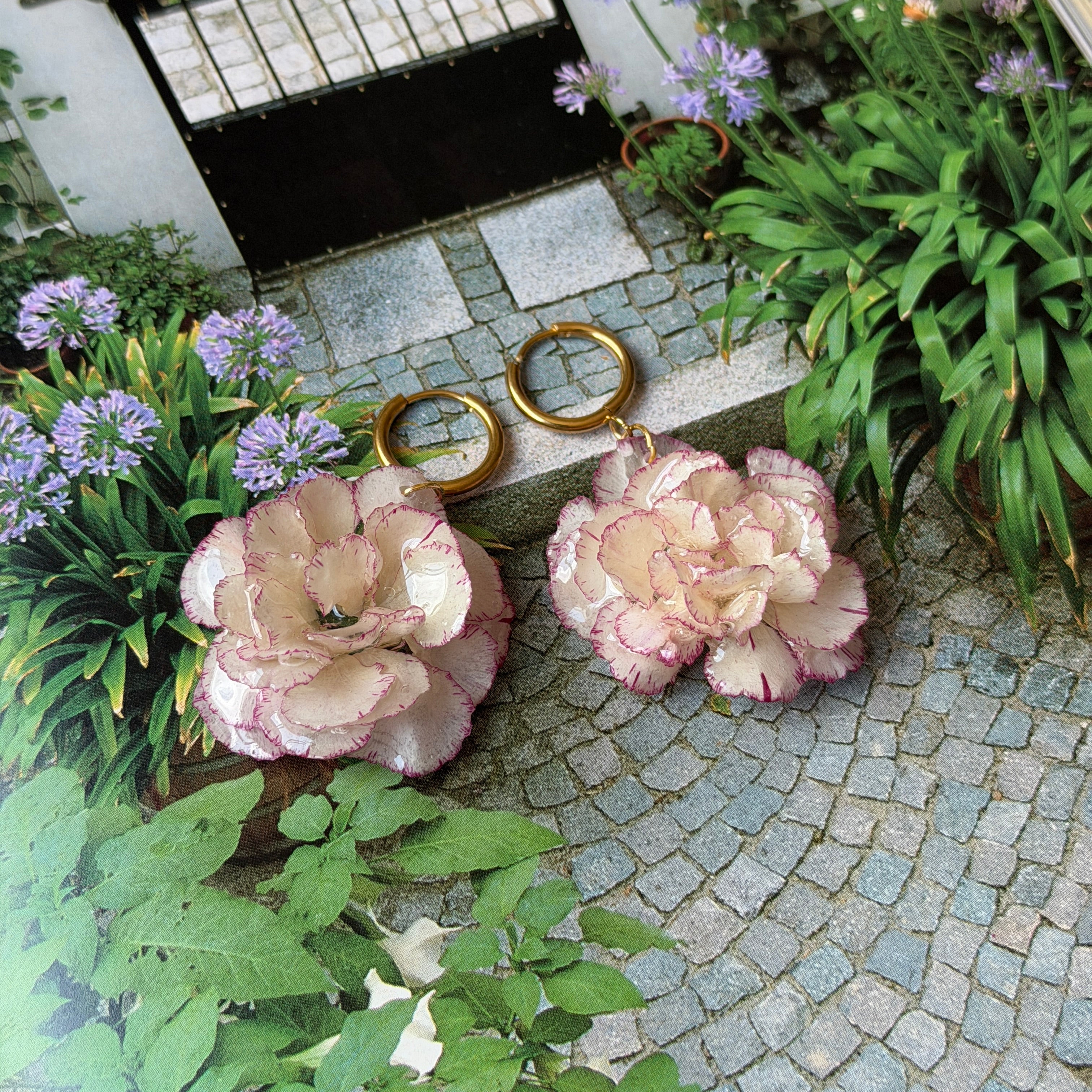 Pendientes de clavel marfil y rosa claro encapsulado en resina sobre una página de jardín