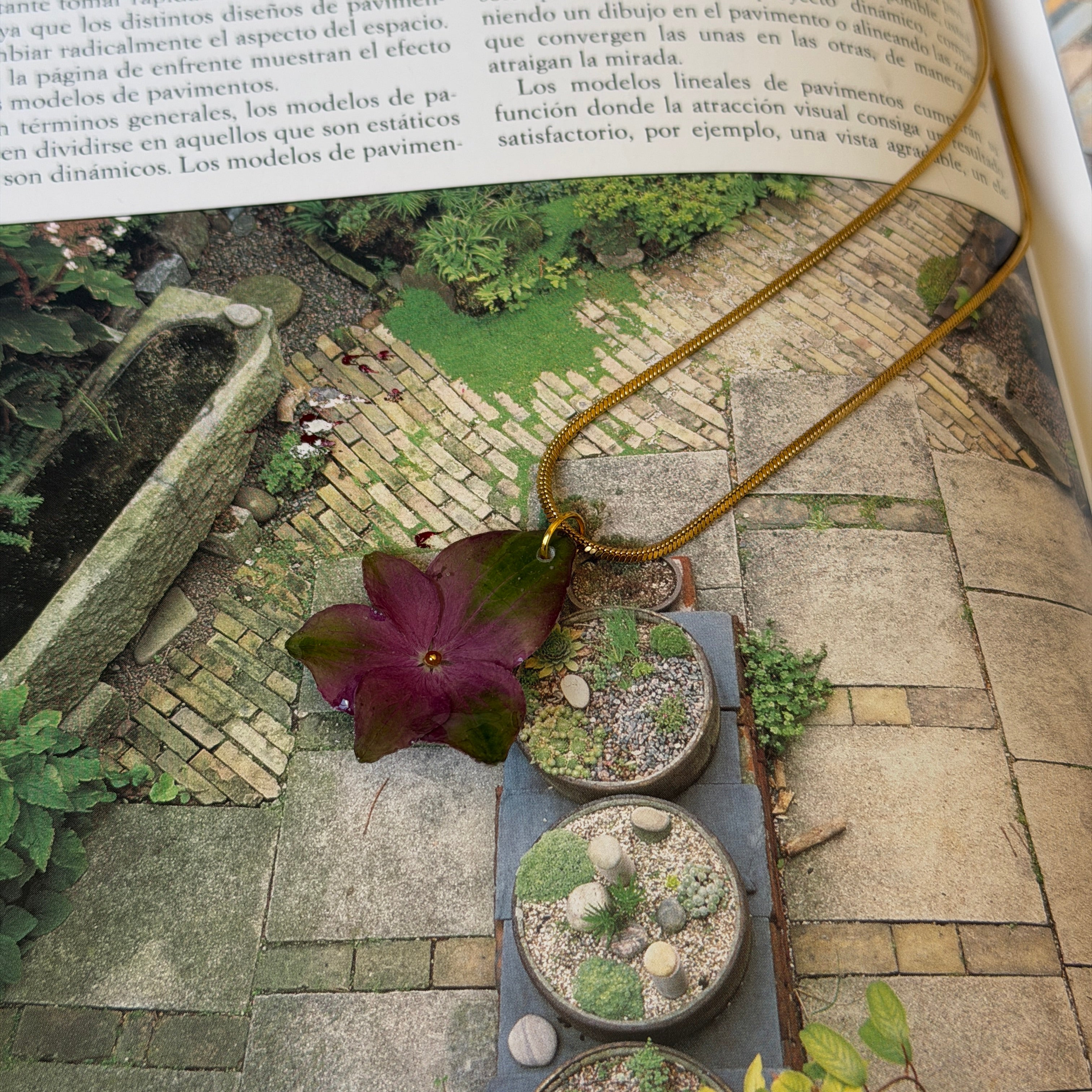 Collar de hortensia morada y verde encapsulada en resina sobre un libro abierto