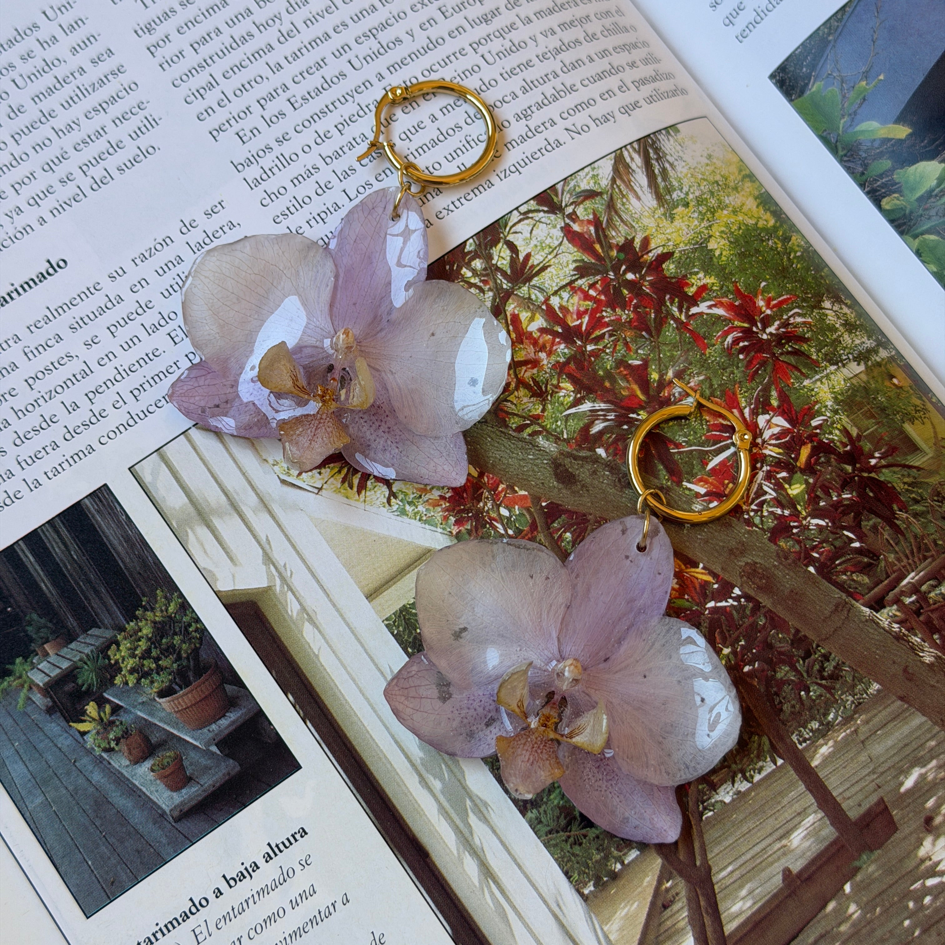 Pendientes de orquídea lila encapsulada en resina sobre una revista