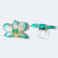 Anillo con orquídea turquesa encapsulada en resina, vista frontal y de perfil sobre aro de acero inoxidable