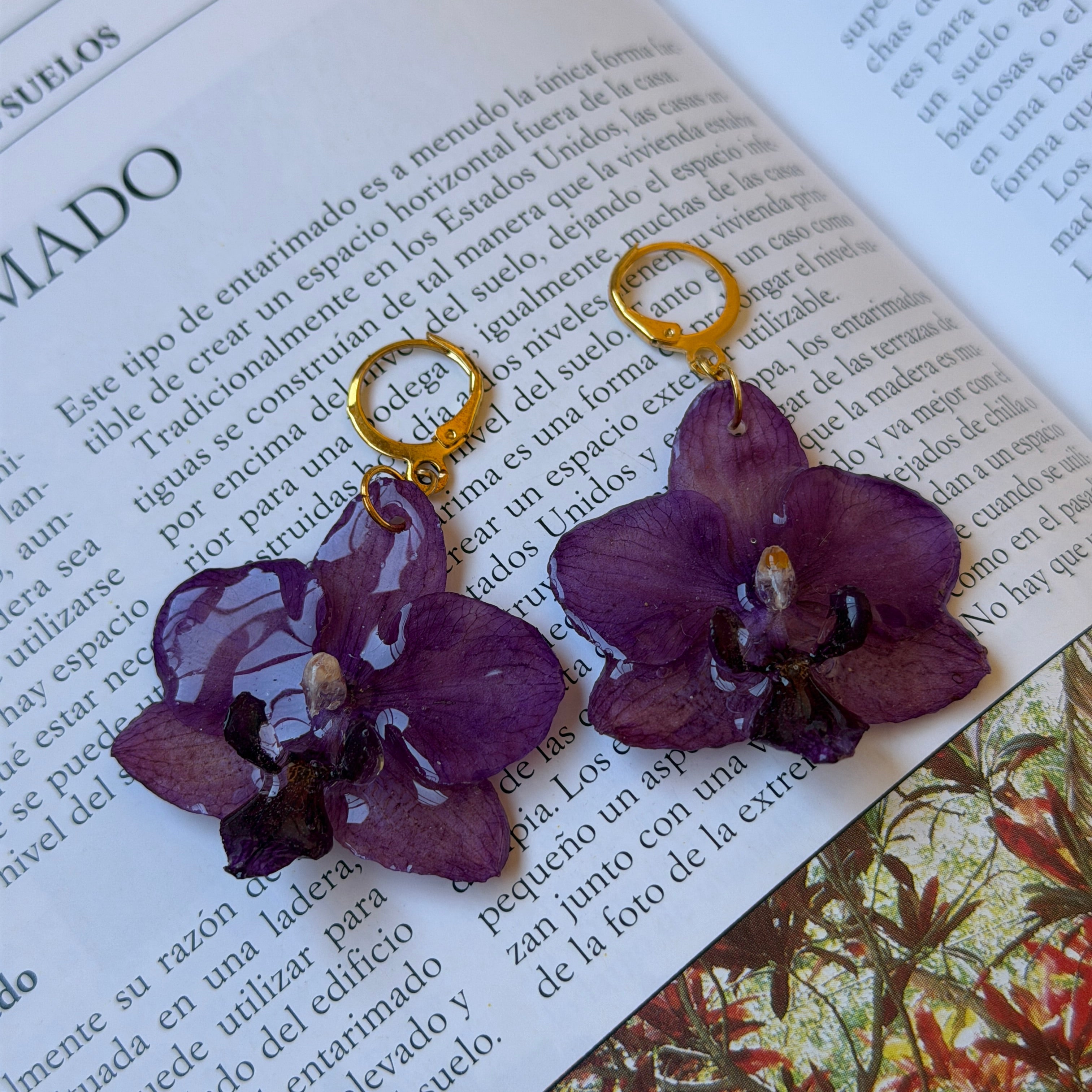 Pendientes de orquídea púrpura encapsulada en resina sobre una revista