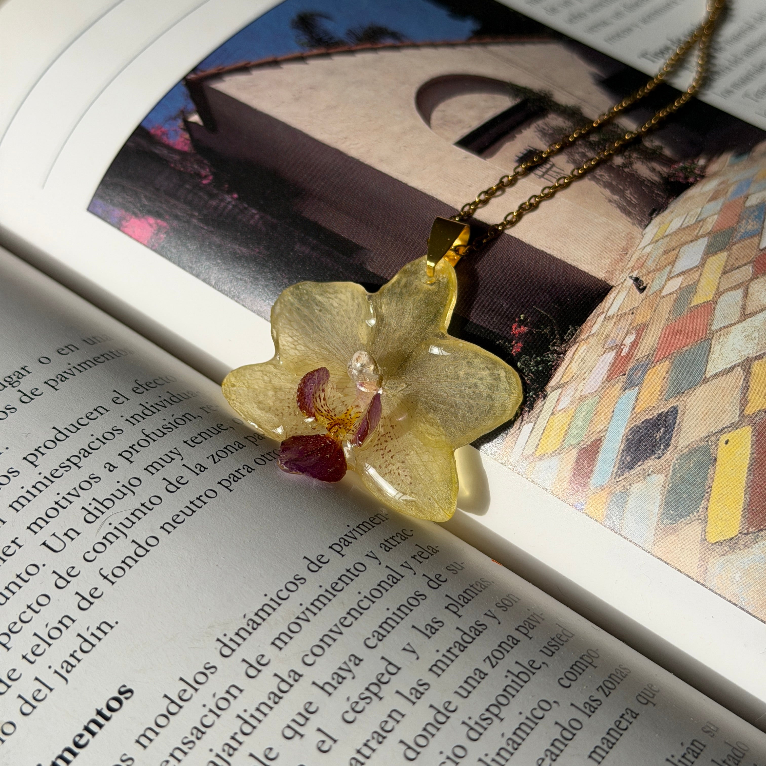 Collar con orquídea amarillo mantequilla y labelo burdeos encapsulada en resina, sobre revista abierta