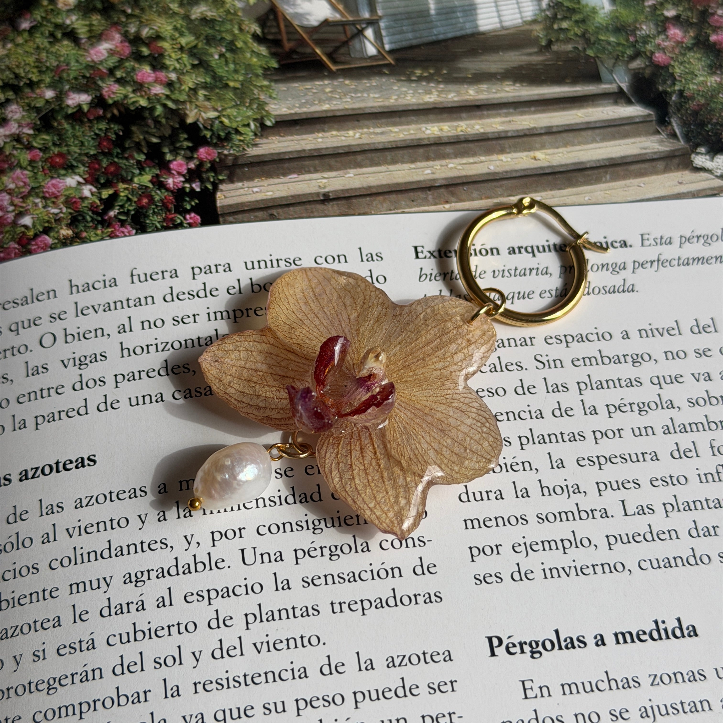 Detalle de orquídea marfil tostado real preservada en resina, centro burdeos y perla natural de agua dulce
