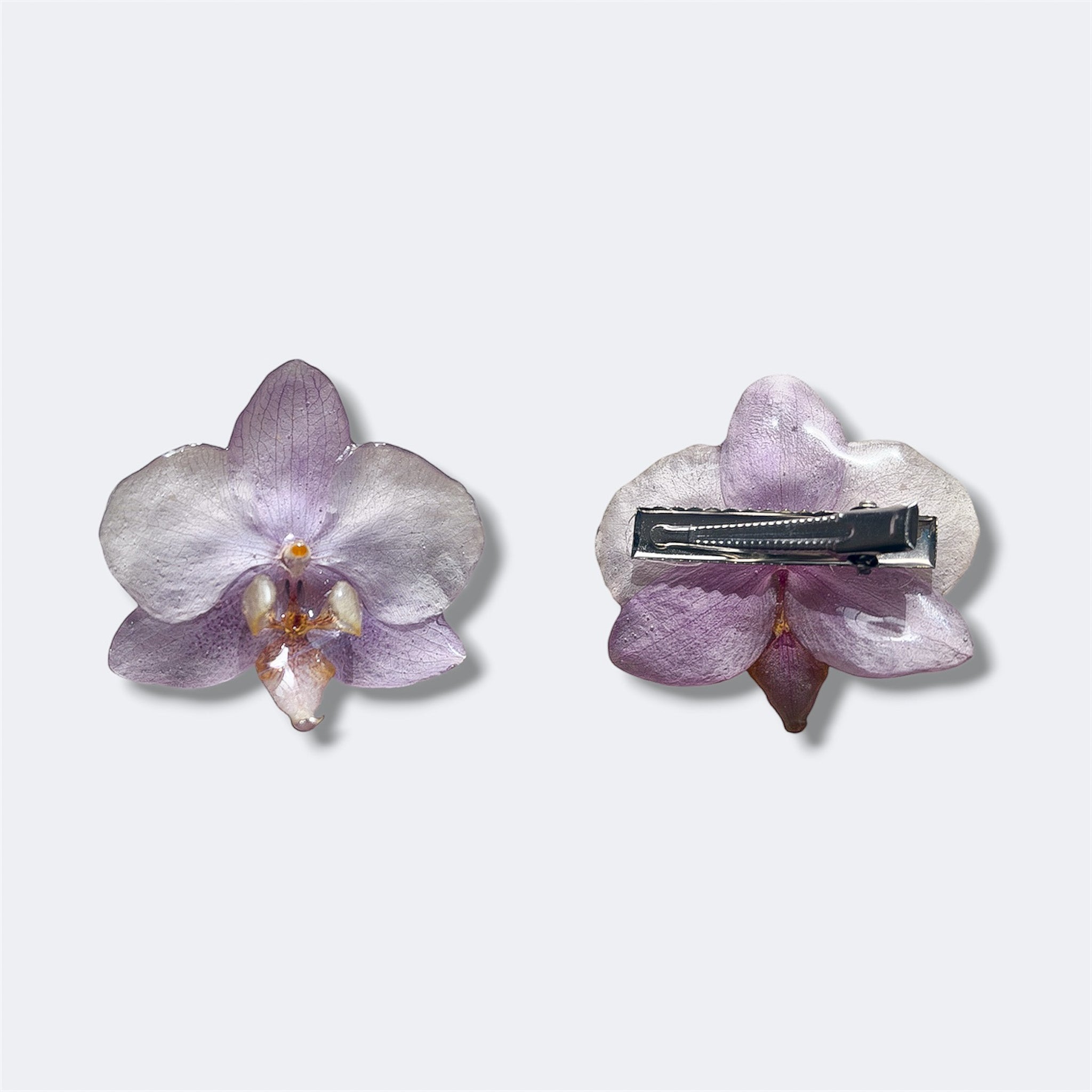 Pinza con orquídea lavanda encapsulada en resina sobre cocodrilo plateado, vista frontal y trasera