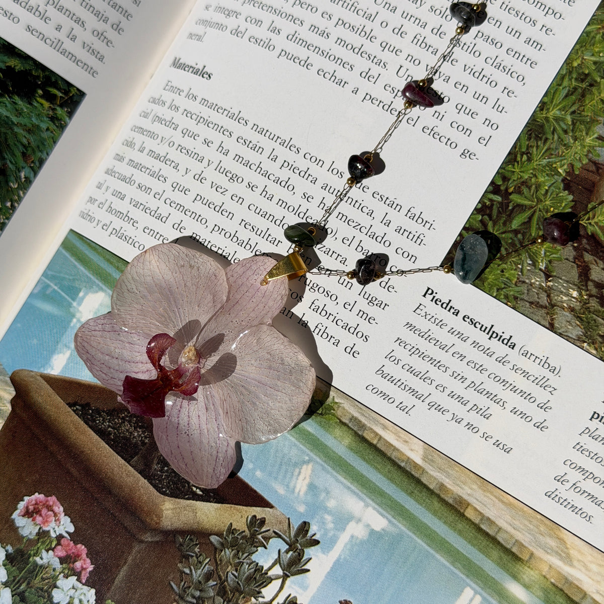 Collar de orquídea blanca con cadena de piedras naturales sobre las páginas de un libro abierto