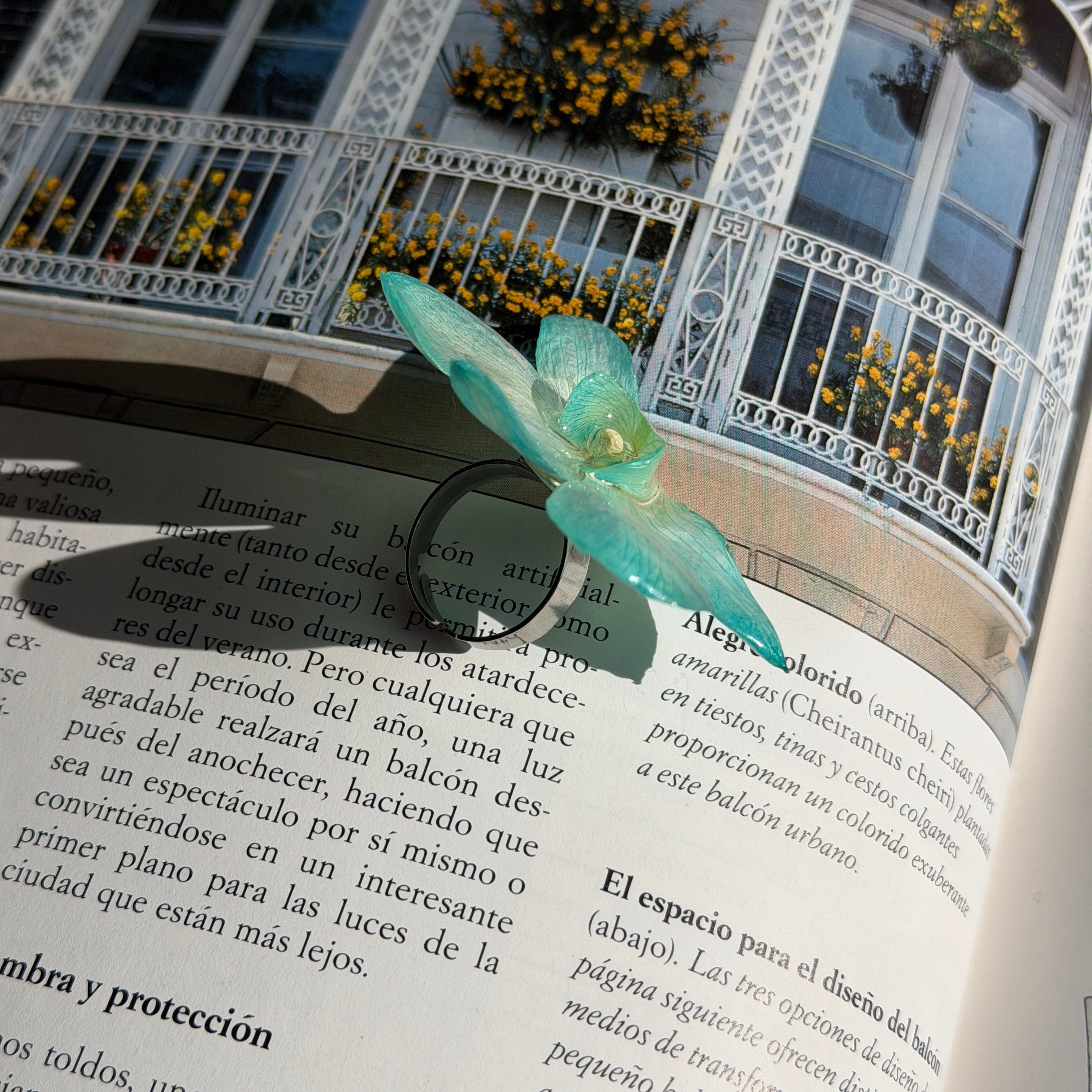 Anillo de orquídea turquesa encapsulada en resina apoyado sobre un libro abierto