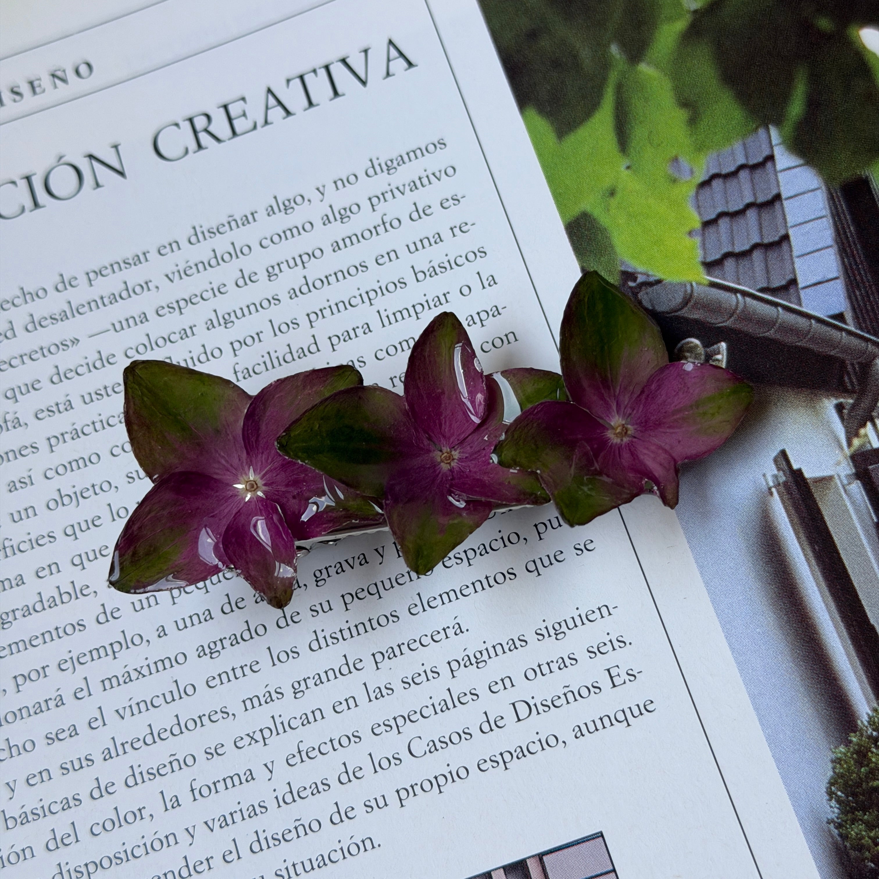 Pinza de tres hortensias fucsia y verde en resina sobre una revista de diseño