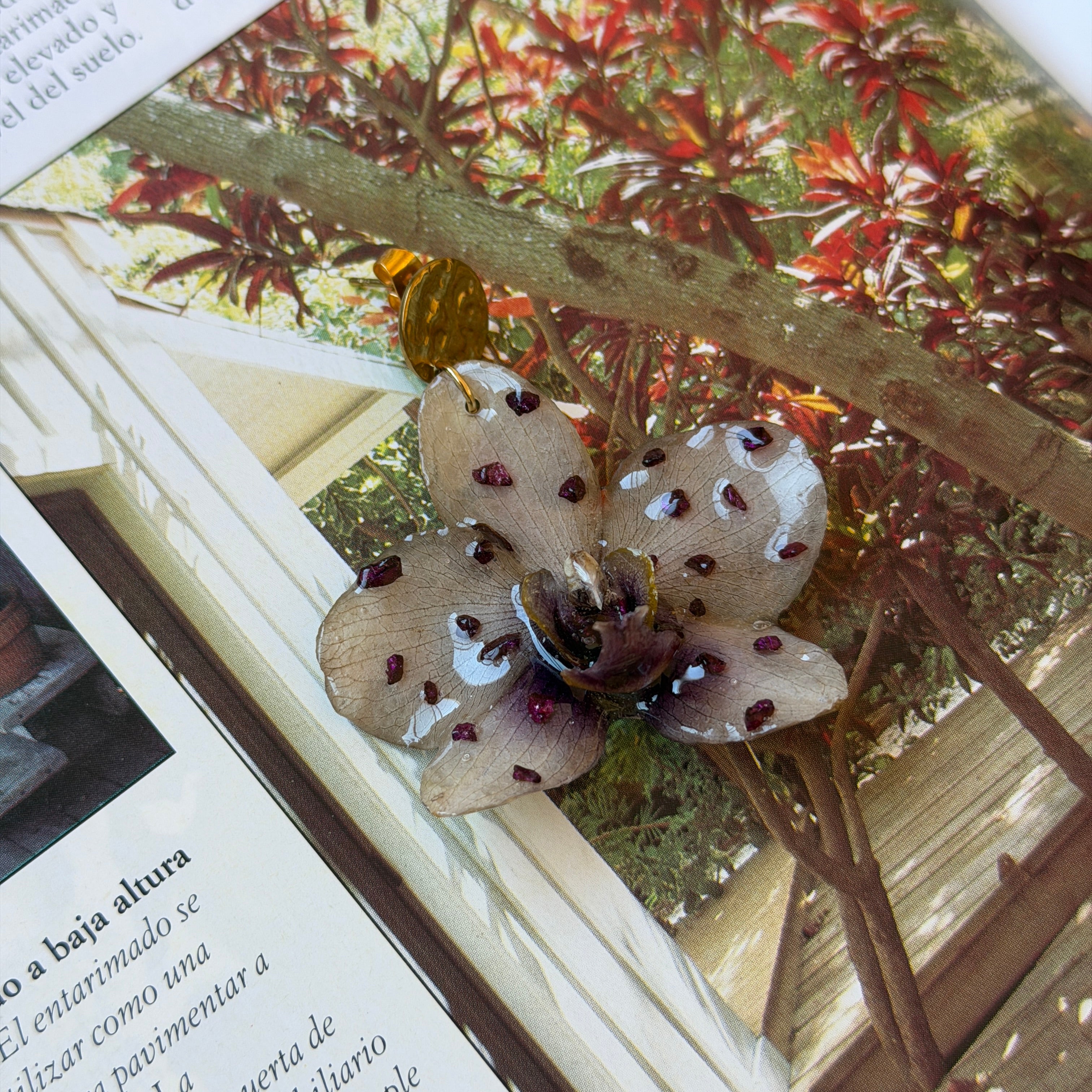 Pendiente con orquídea beige moteada real preservada en resina, sobre madera al aire libre