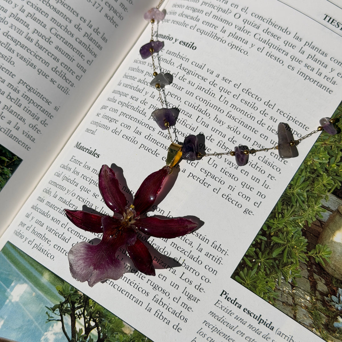 Collar de orquídea Cambria burdeos con cadena de amatistas sobre las páginas de un libro abierto al sol