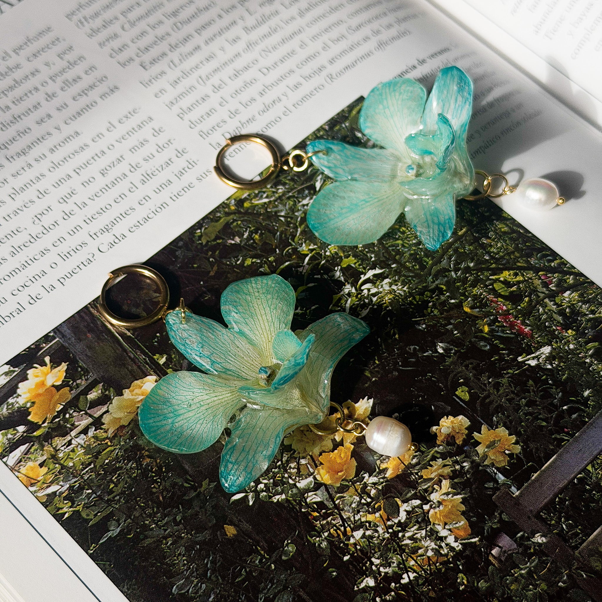 Pendientes de orquídea Dendrobium turquesa encapsulada en resina sobre las páginas de un libro de botánica