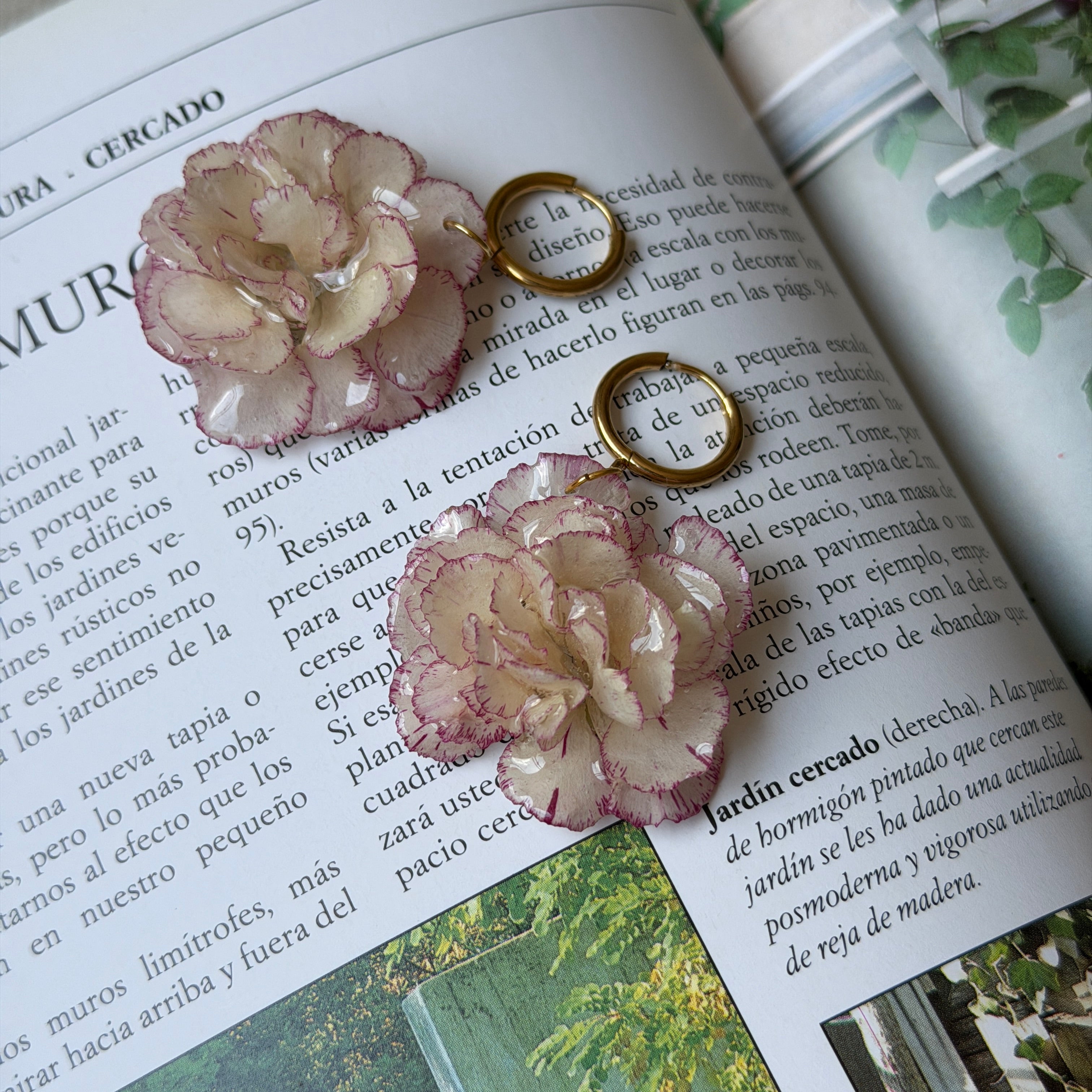 Pendientes de clavel marfil y rosa claro encapsulado en resina sobre las páginas de una revista