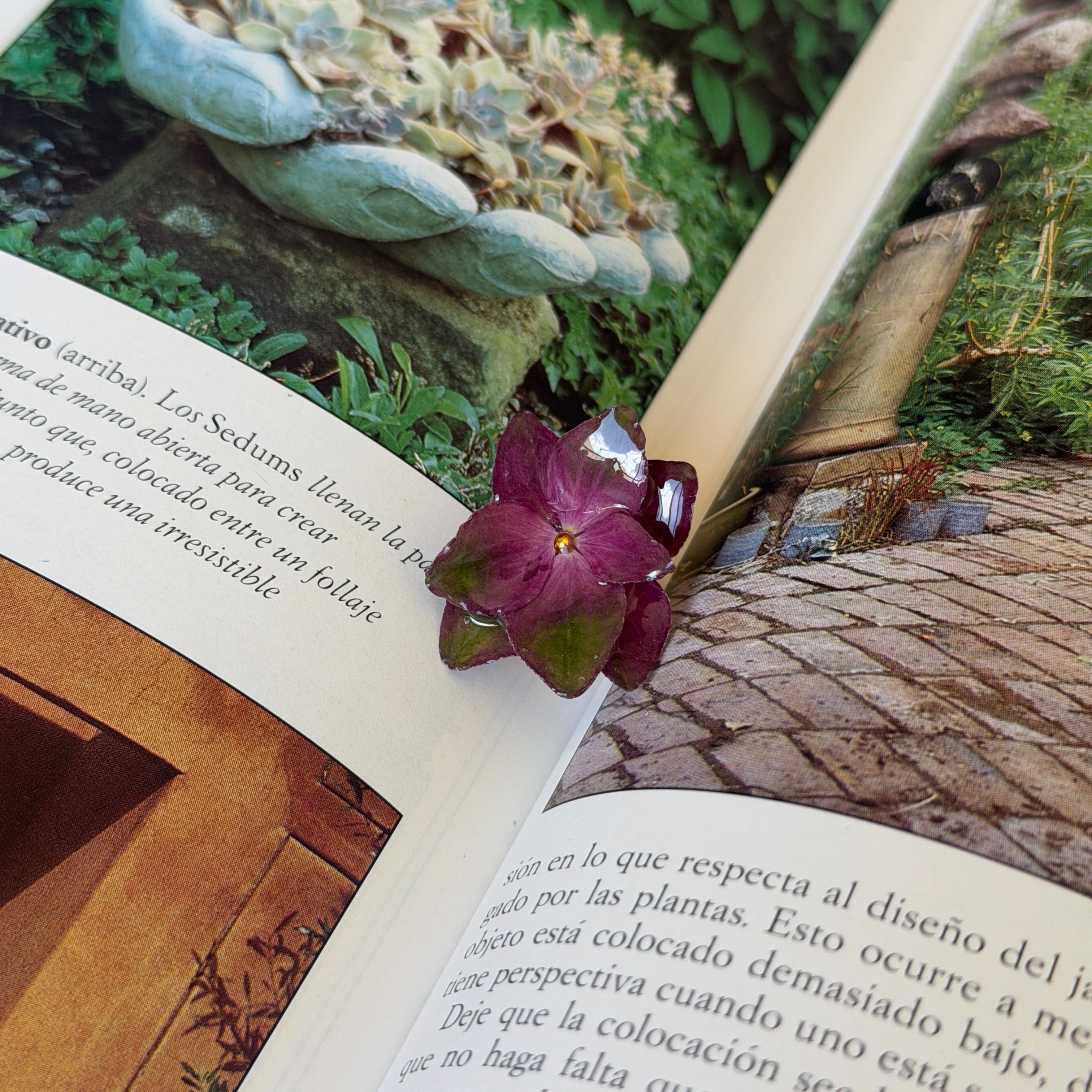 Anillo de hortensias magenta y verdes encapsuladas en resina sobre un libro de jardinería abierto