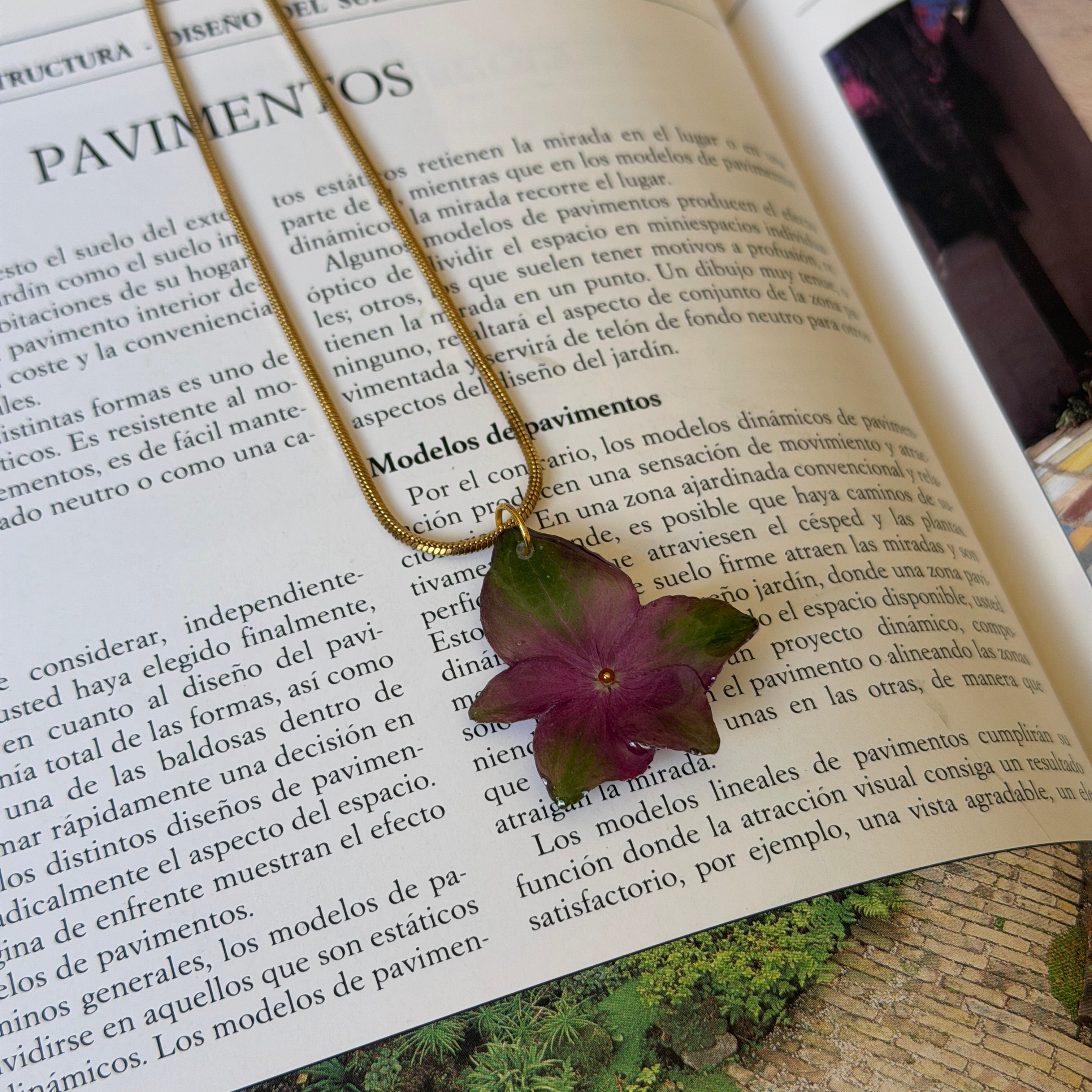 Collar de hortensia morada y verde encapsulada en resina sobre un libro de diseño de jardines