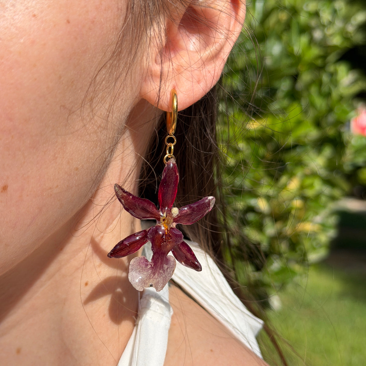 Detalle del pendiente de orquídea Cambria burdeos colgando del aro sobre la oreja