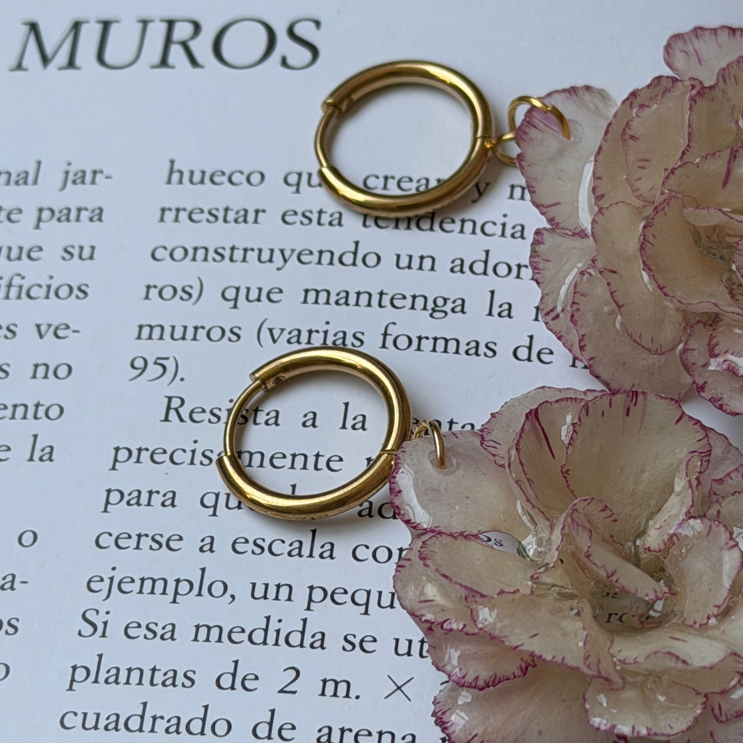 Detalle de clavel marfil real preservado en resina, con borde dentado rosa claro y aro de acero inoxidable