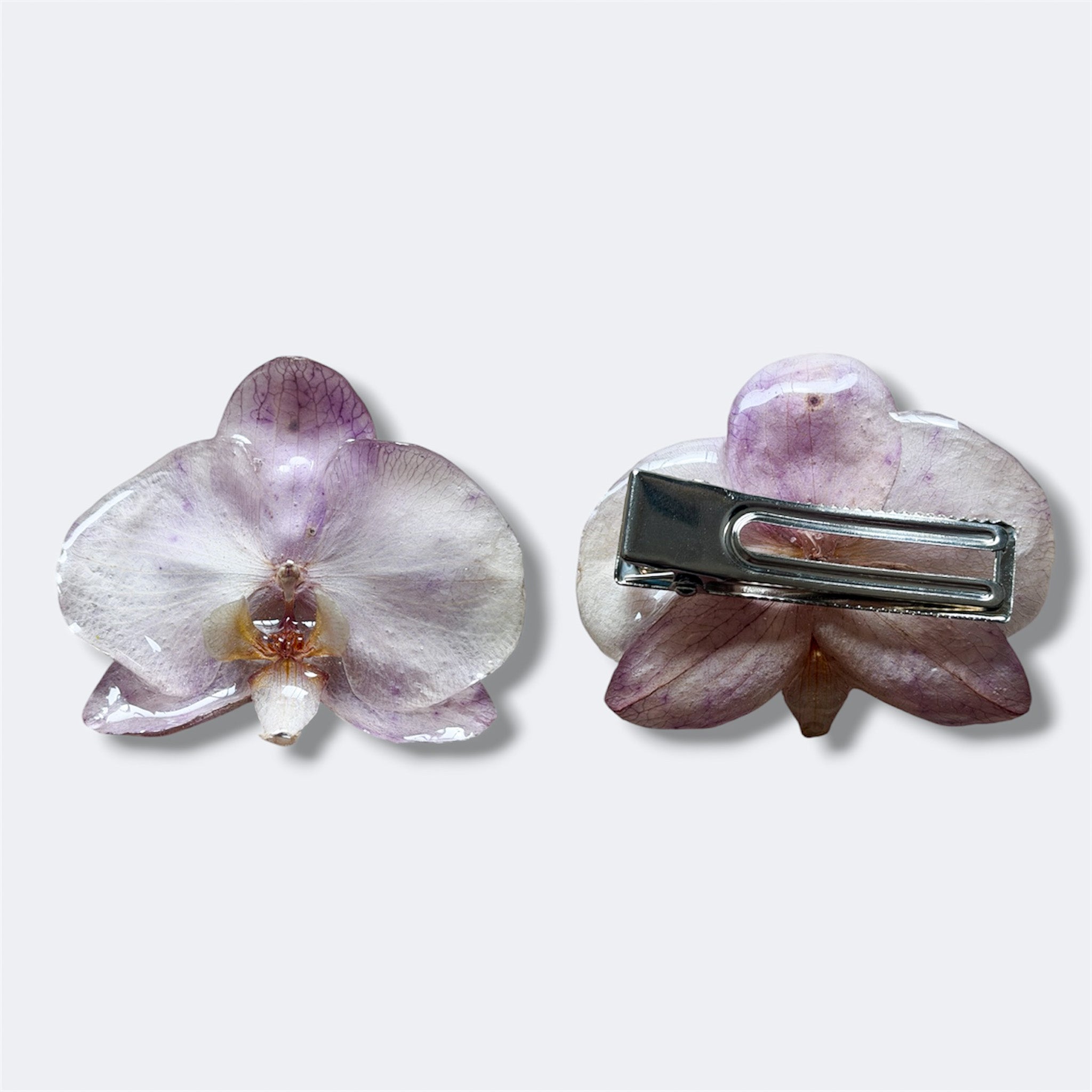 Pinza con orquídea lavanda encapsulada en resina, anverso y pinza de cocodrilo plateada al dorso