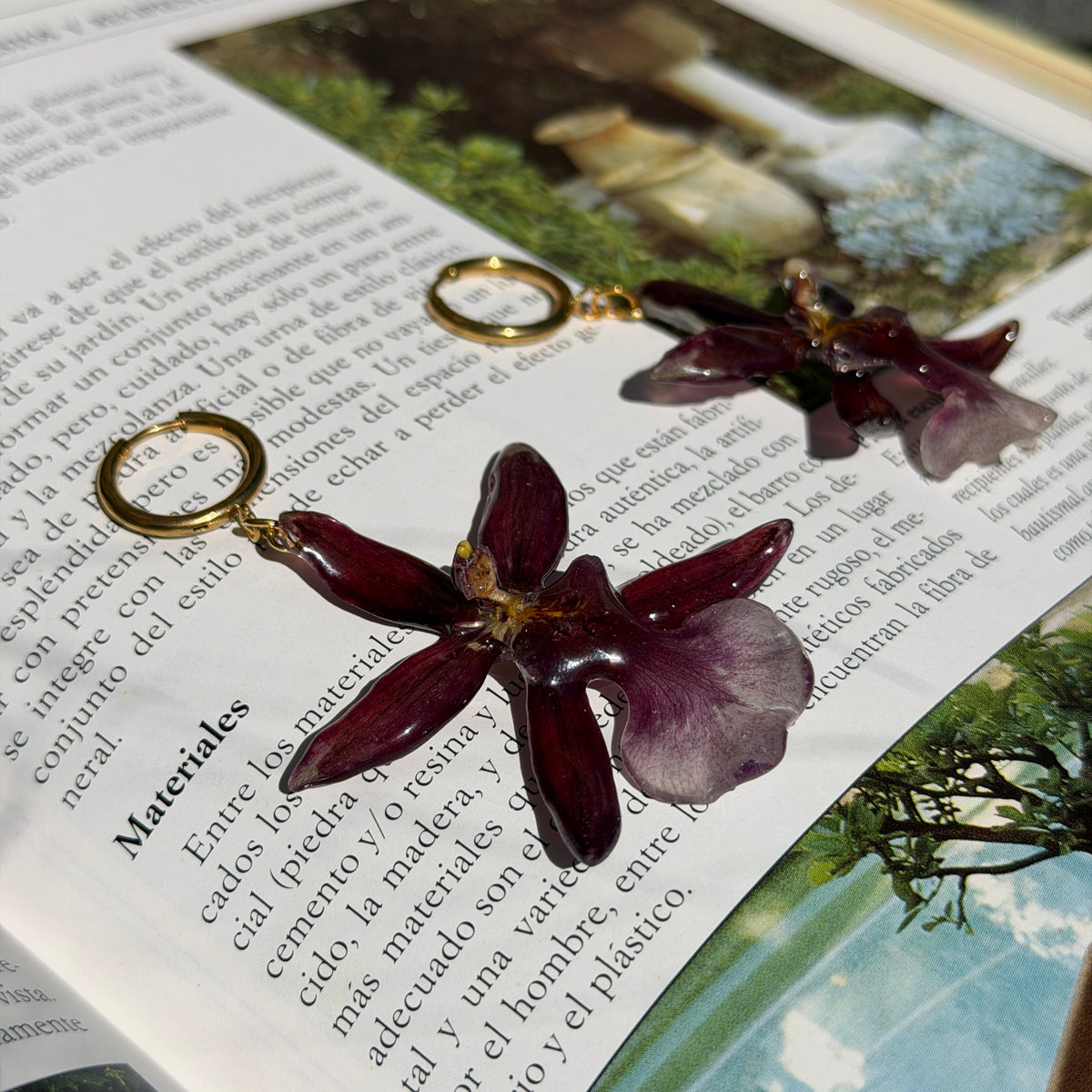 Pendientes de orquídea Cambria burdeos encapsulada en resina sobre las páginas de un libro abierto