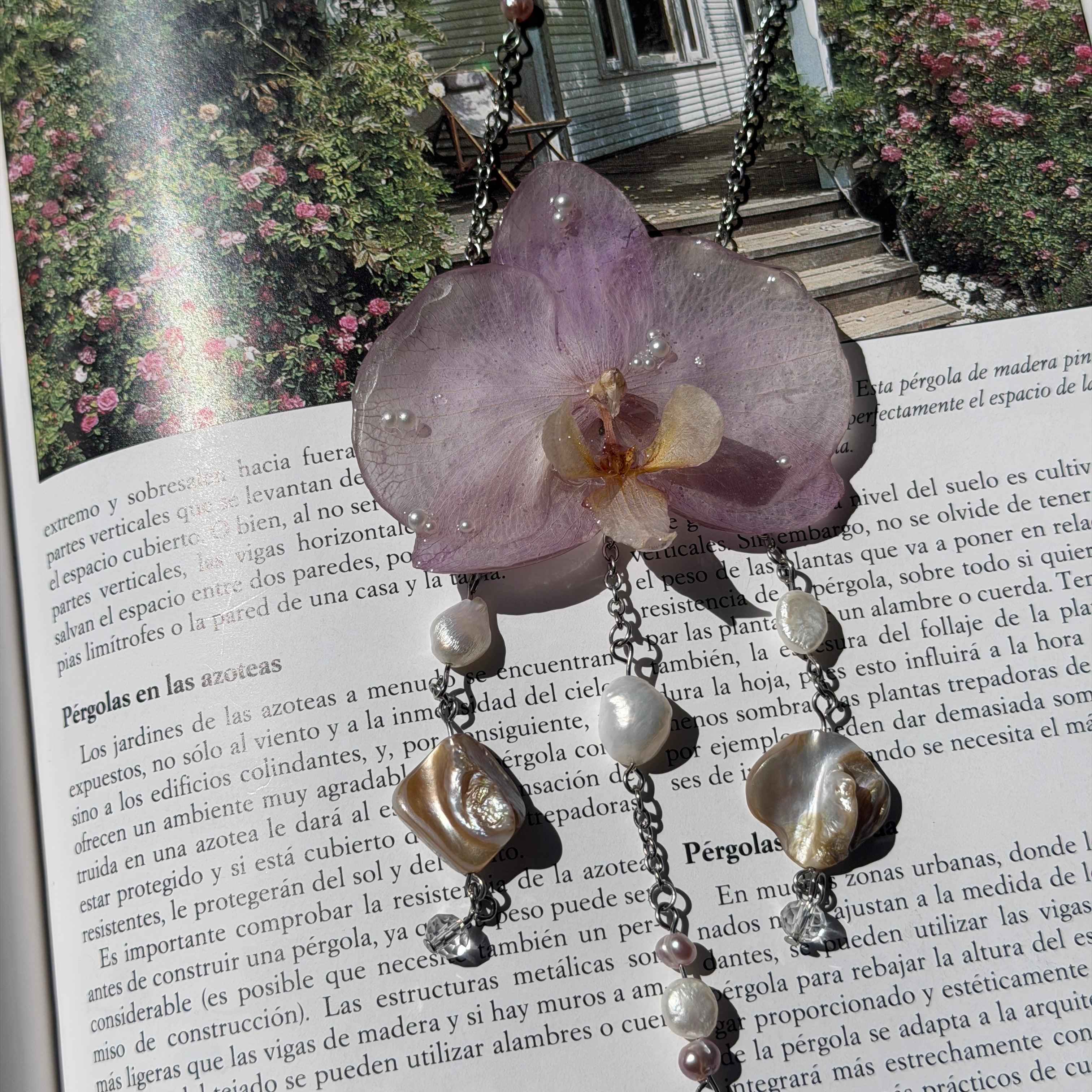 Collar de orquídea lila encapsulada en resina sobre un libro abierto, con las caídas de perlas extendidas