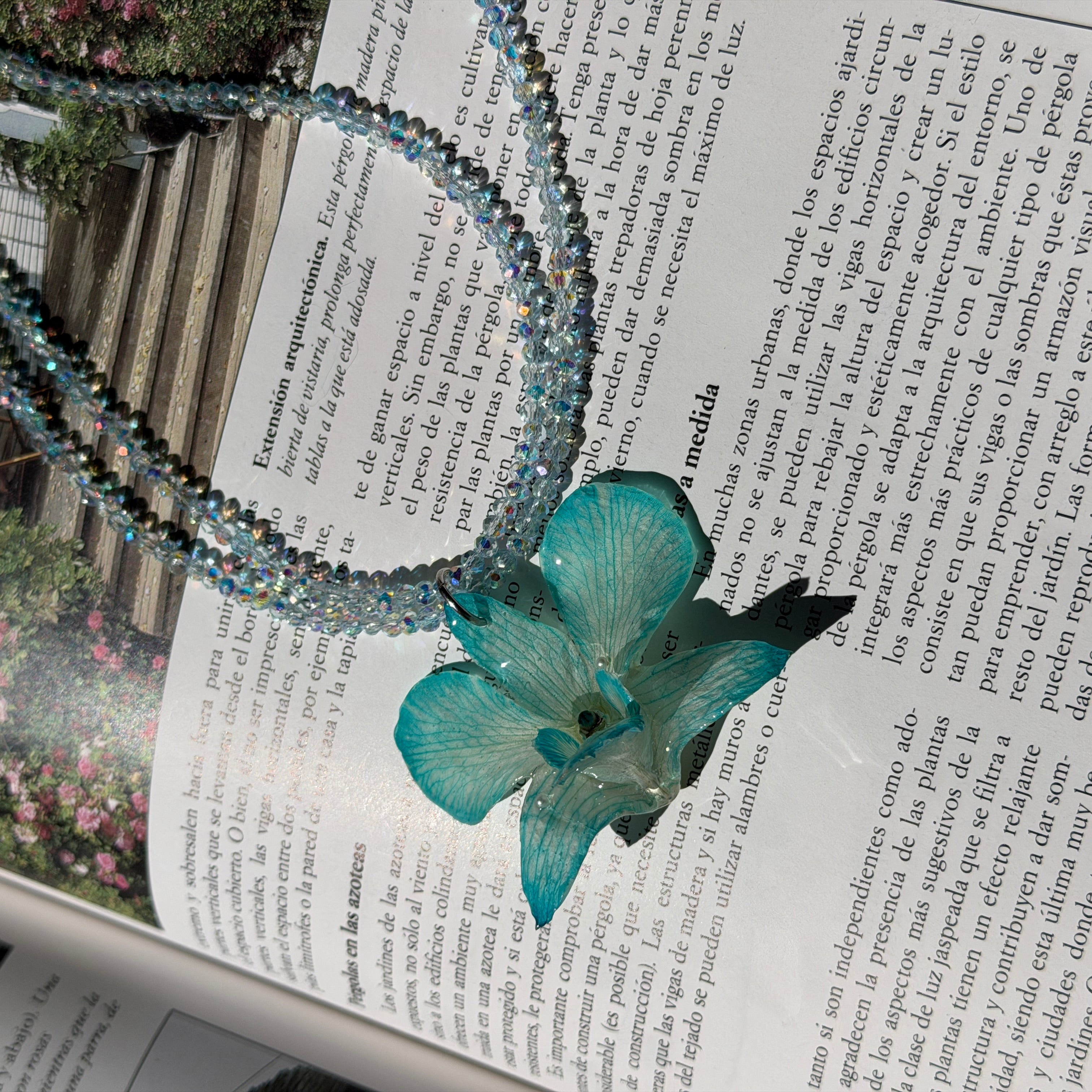Collar de orquídea turquesa encapsulada en resina sobre las páginas abiertas de una revista