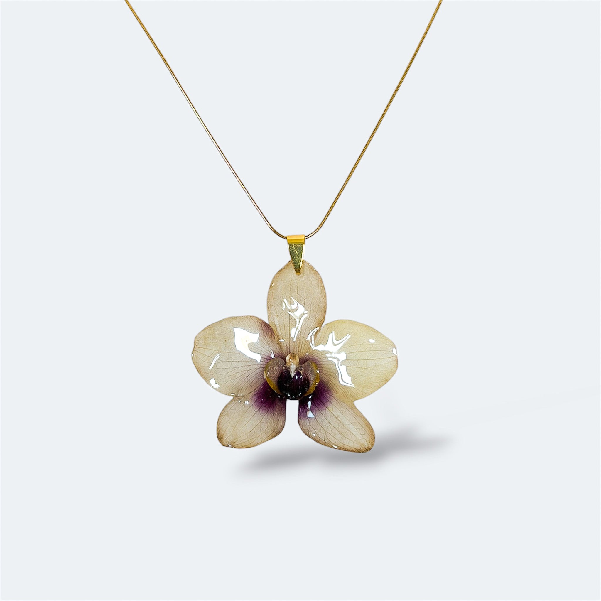 Collar con orquídea blanco crema encapsulada en resina, sobre cadena fina de acero