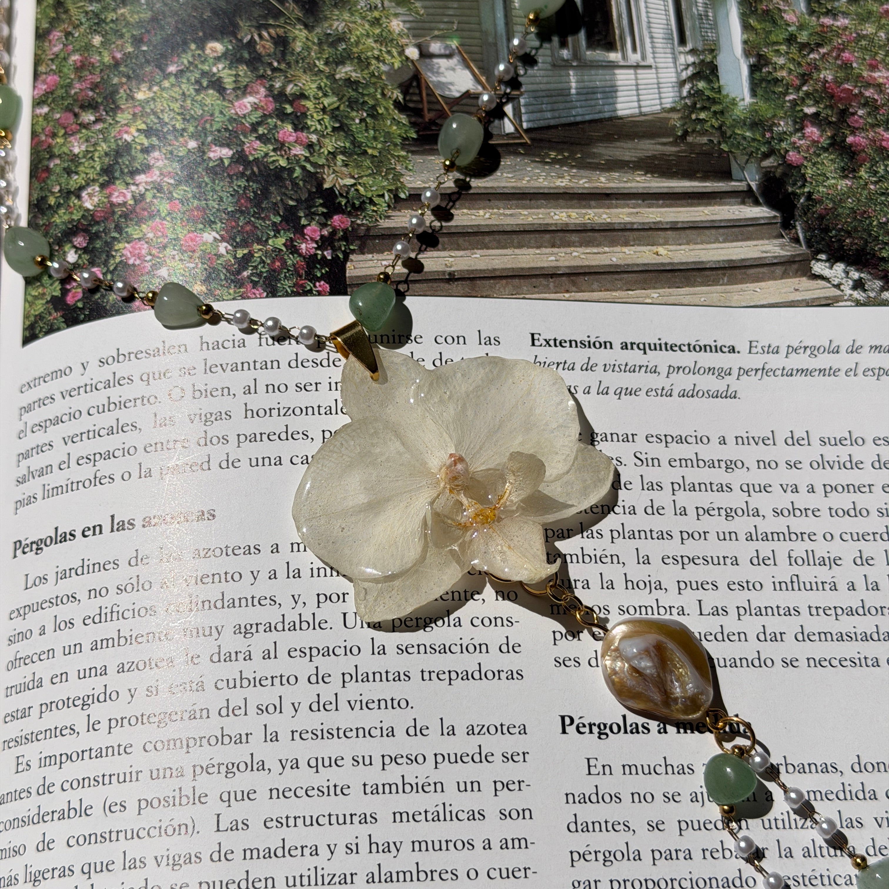 Collar de orquídea blanca en resina con perla barroca y piedras verdes sobre un libro abierto