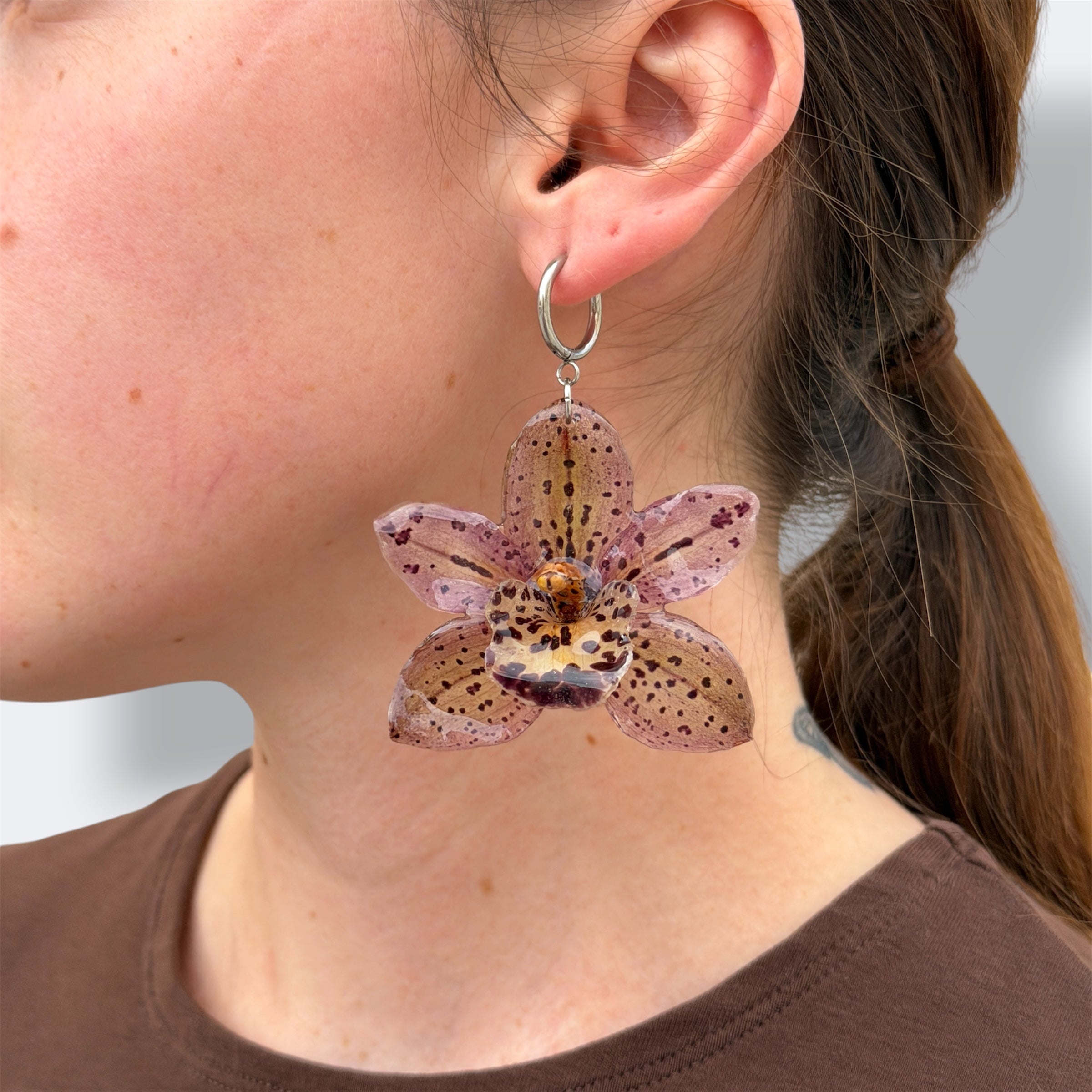 Mujer llevando pendiente de orquídea malva moteada encapsulada en resina sobre la oreja