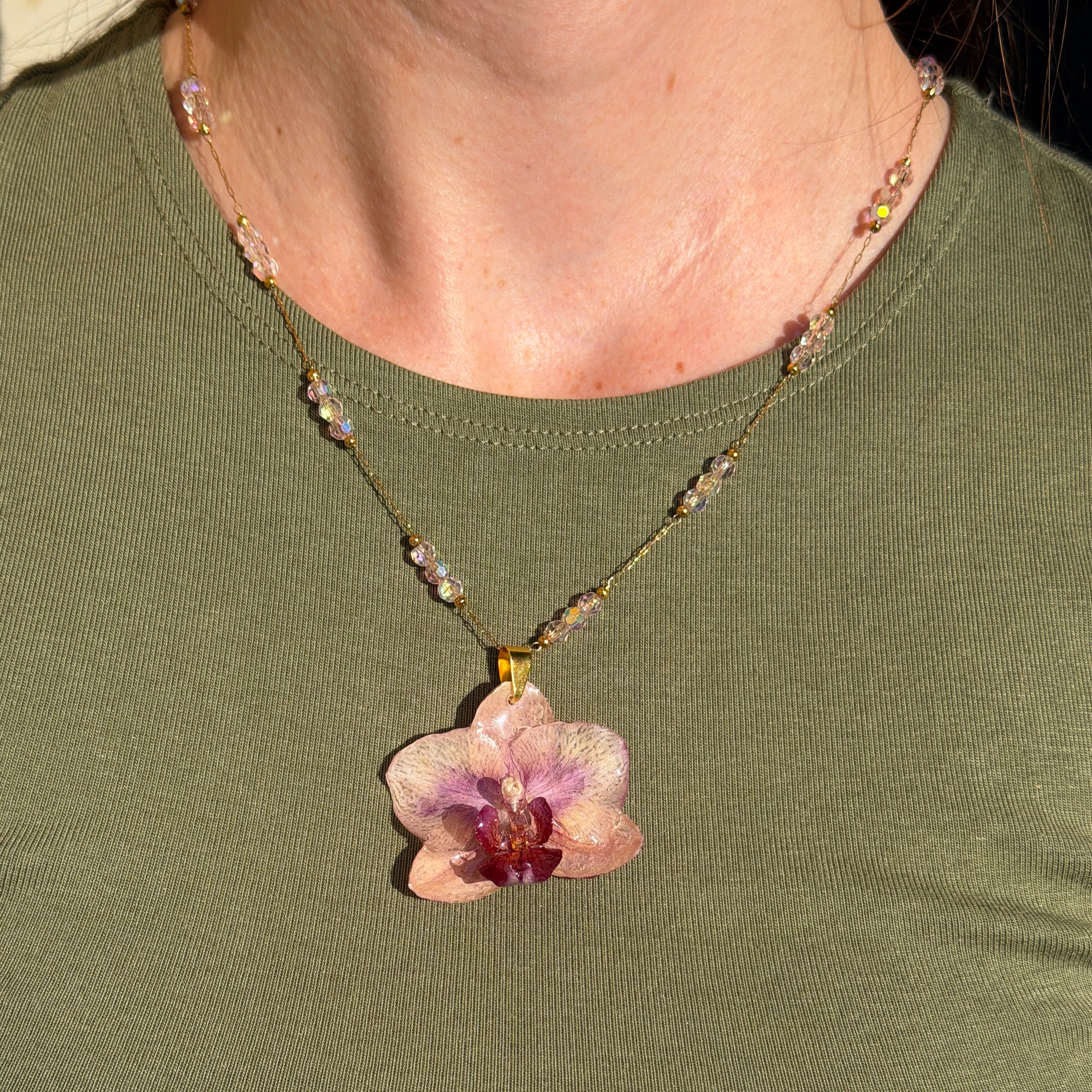 Mujer llevando collar de orquídea rosa encapsulada en resina sobre el escote