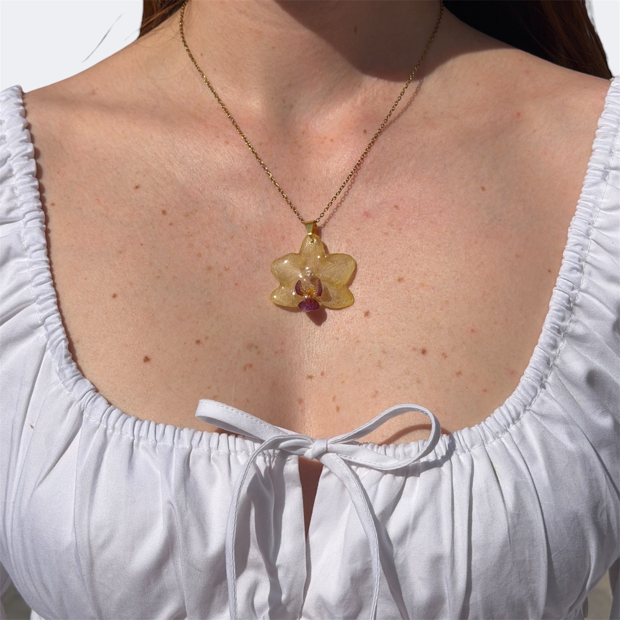 Mujer llevando collar de orquídea amarillo mantequilla encapsulada en resina sobre el escote