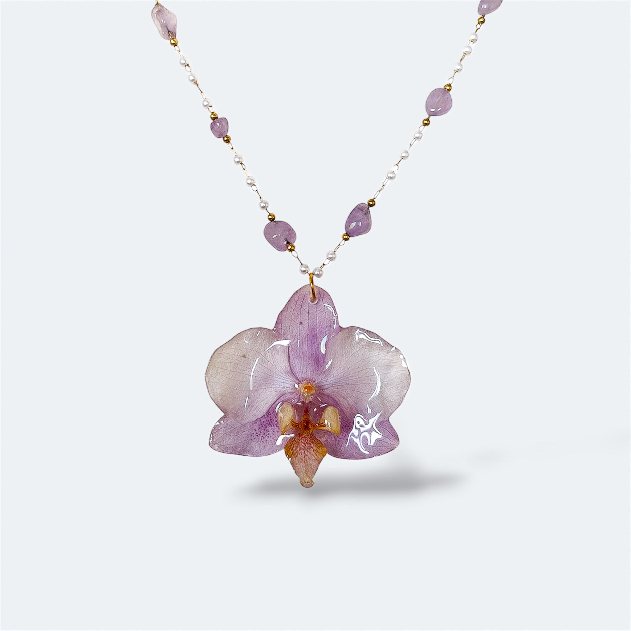 Collar con orquídea lila encapsulada en resina, sobre cadena de acero con perlas y amatista