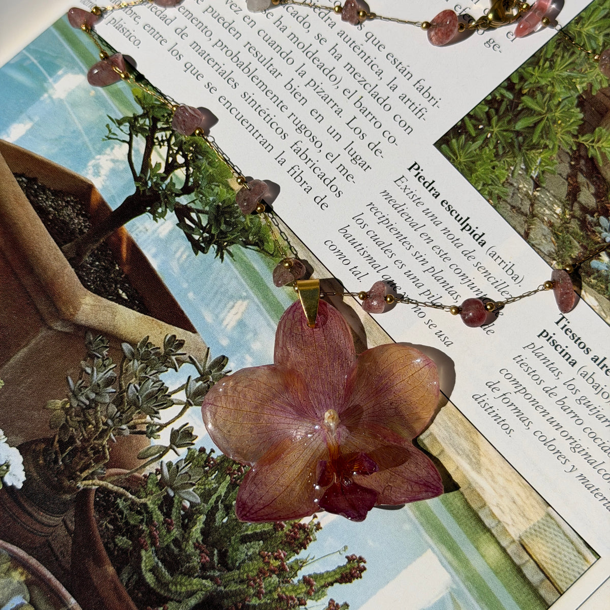 Collar de orquídea rosa terroso encapsulada en resina sobre las páginas de un libro abierto