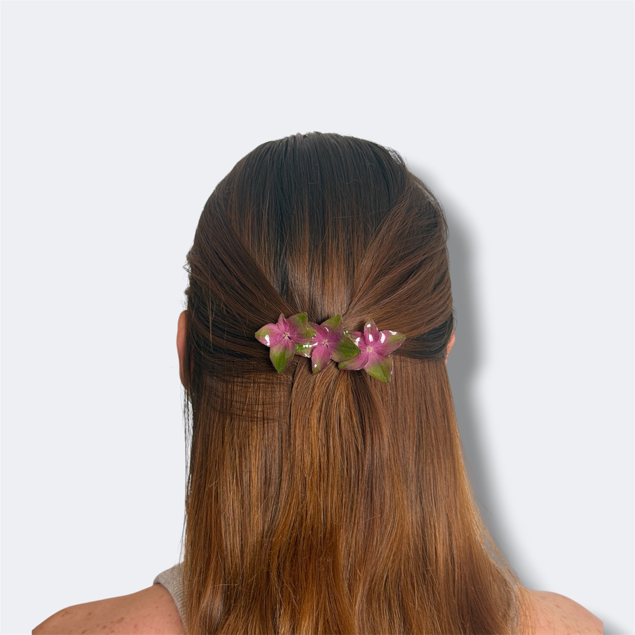 Mujer llevando pinza de hortensias fucsia y verde encapsuladas en resina en el pelo