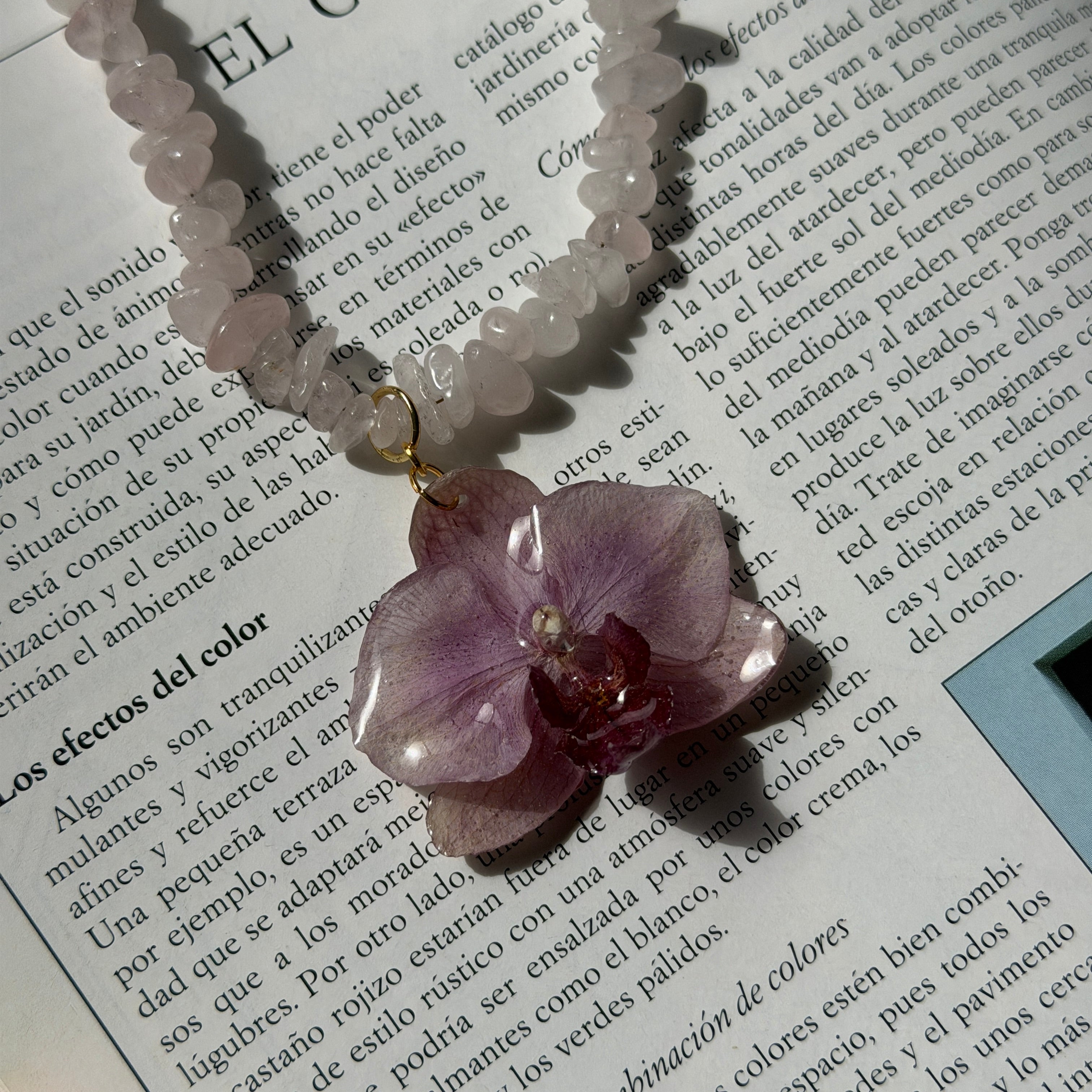 Colgante de orquídea violeta real preservada en resina sobre una revista abierta