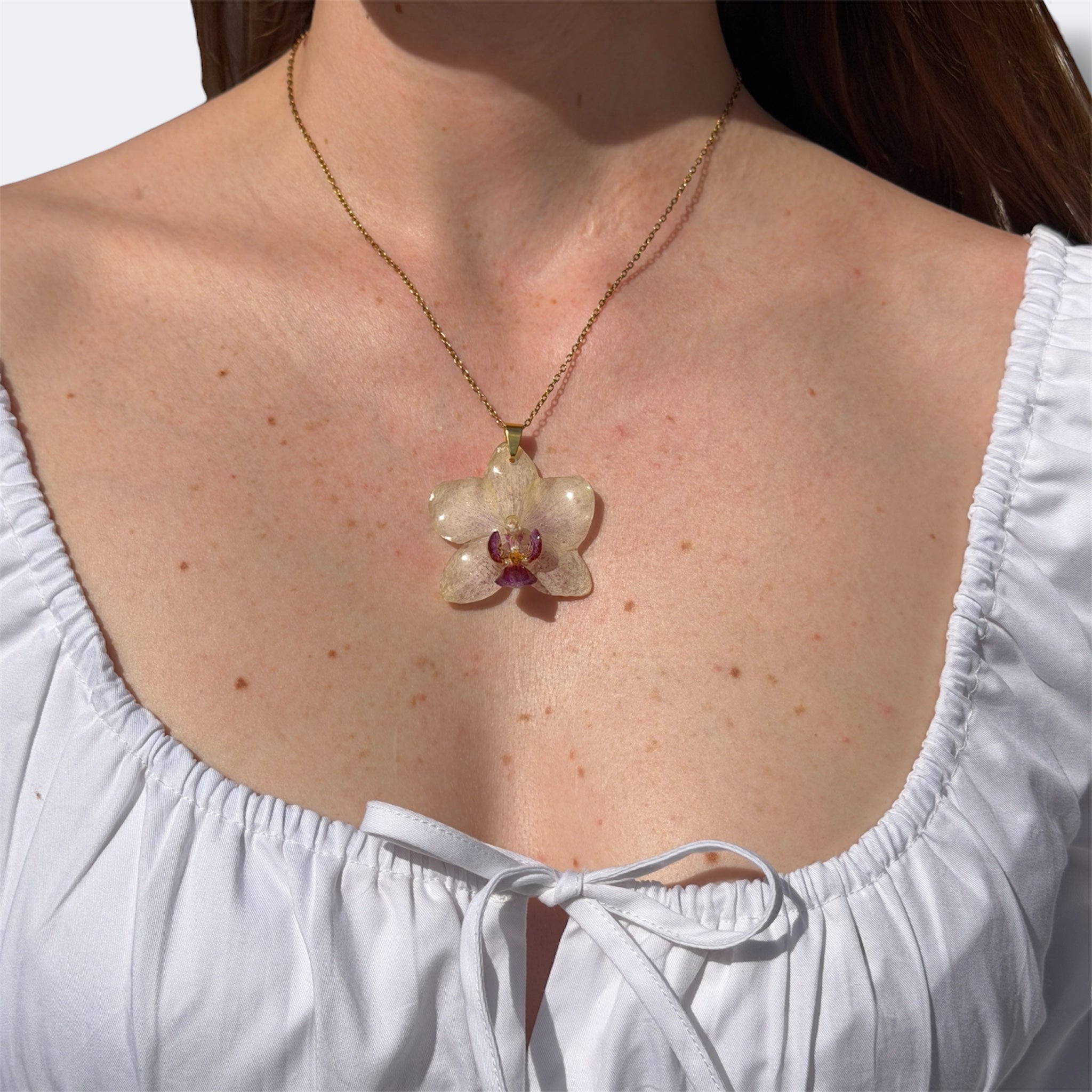 Mujer llevando collar de orquídea blanco marfil encapsulada en resina sobre el escote