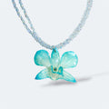 Collar con orquídea turquesa encapsulada en resina, sobre cadena doble de cuentas acrílicas transparentes