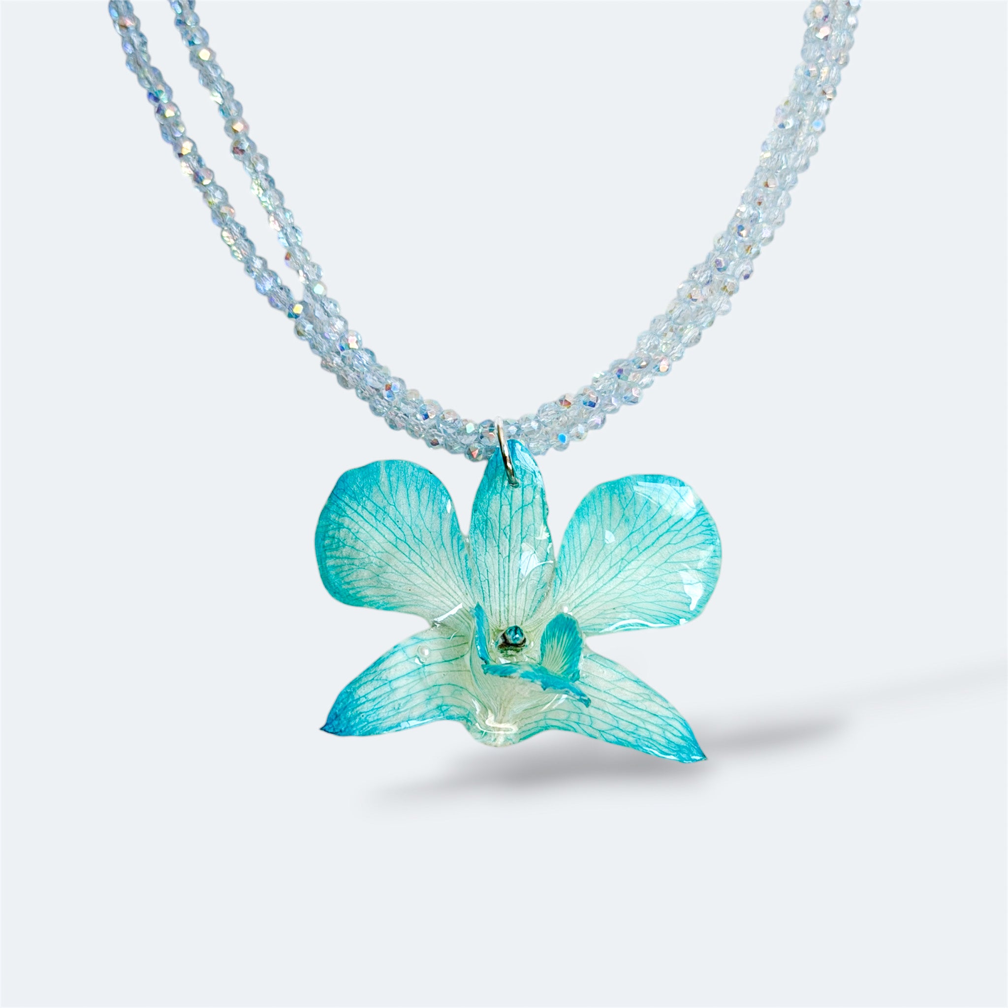 Collar con orquídea turquesa encapsulada en resina, sobre cadena doble de cuentas acrílicas transparentes