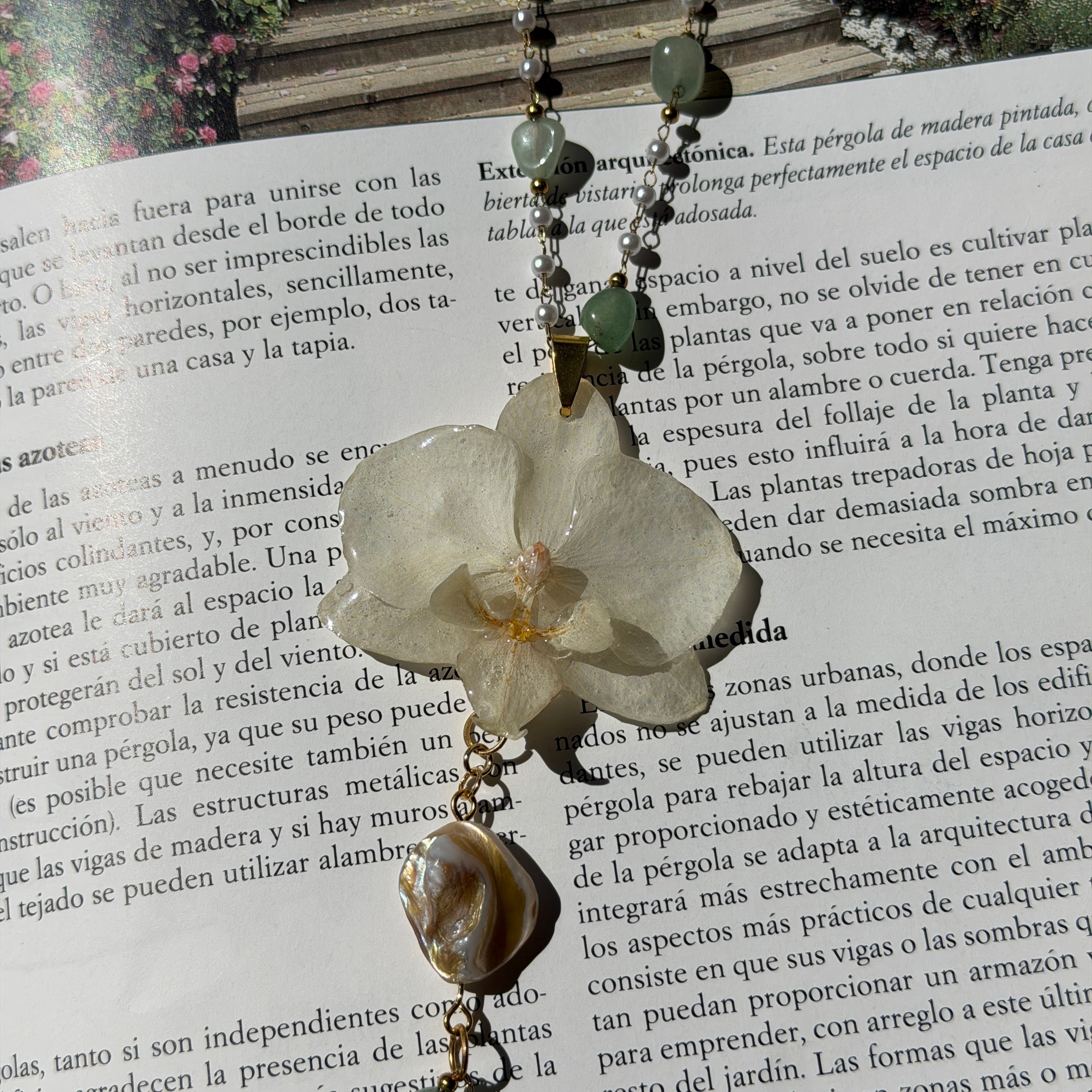 Orquídea blanca encapsulada en resina con perla barroca colgante, a la luz del sol