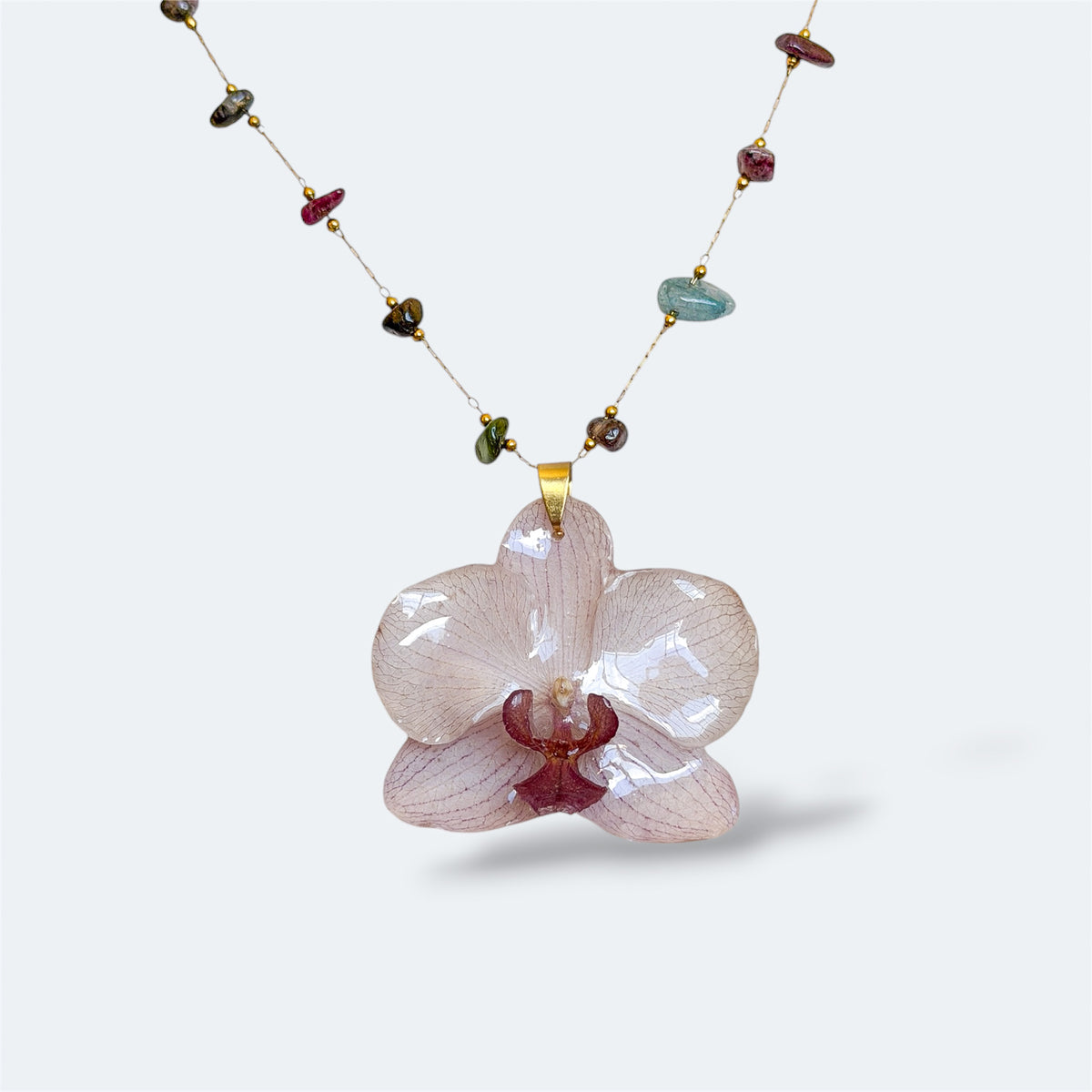 Collar con orquídea blanca encapsulada en resina, sobre cadena de piedras naturales y acero inoxidable