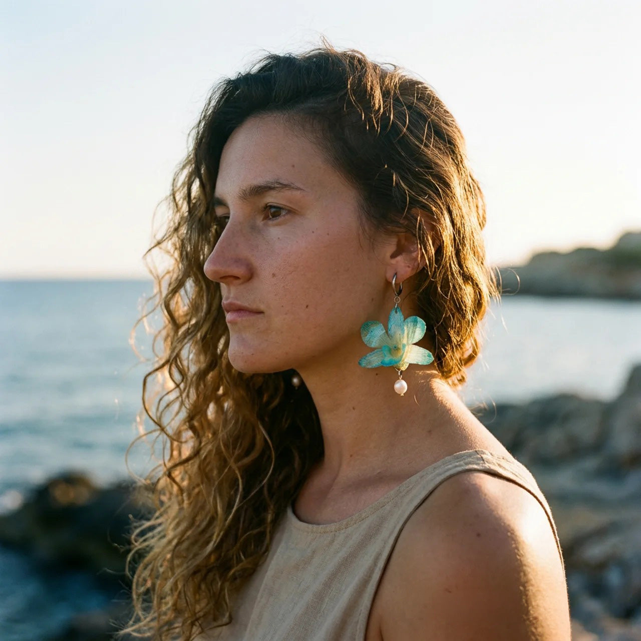 Modelo con pendientes de orquídea turquesa y perla natural en la costa