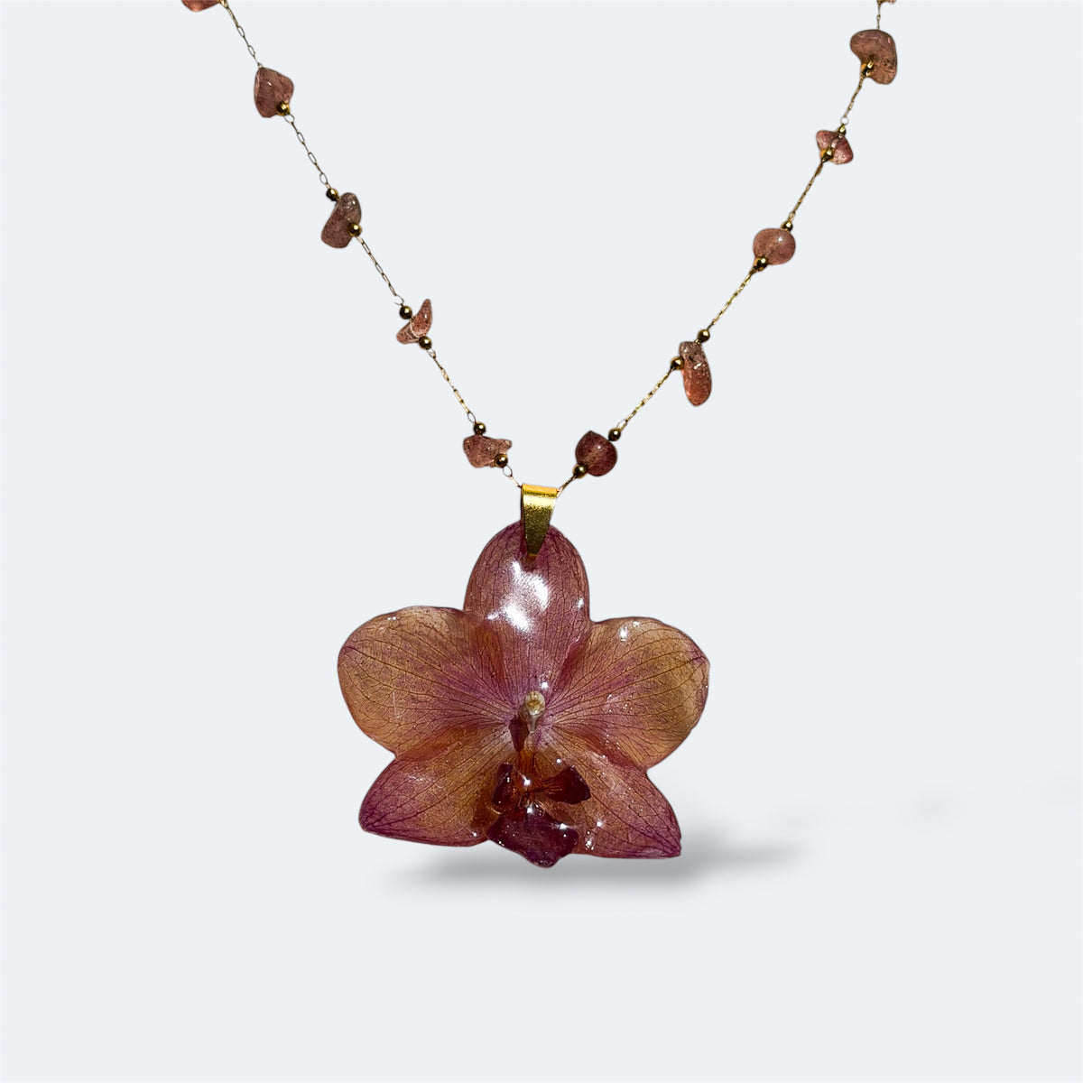 Collar con orquídea rosa terroso encapsulada en resina, sobre cadena de piedras naturales
